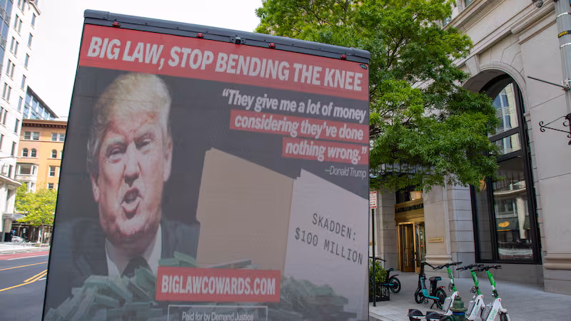A mobile billboard slams law firms who made a deal with Trump, calling on Big Law to "stop bending the knee."