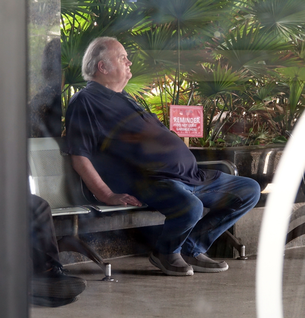 Thomas Markle Sr. resting on a bench with lush greenery and a 