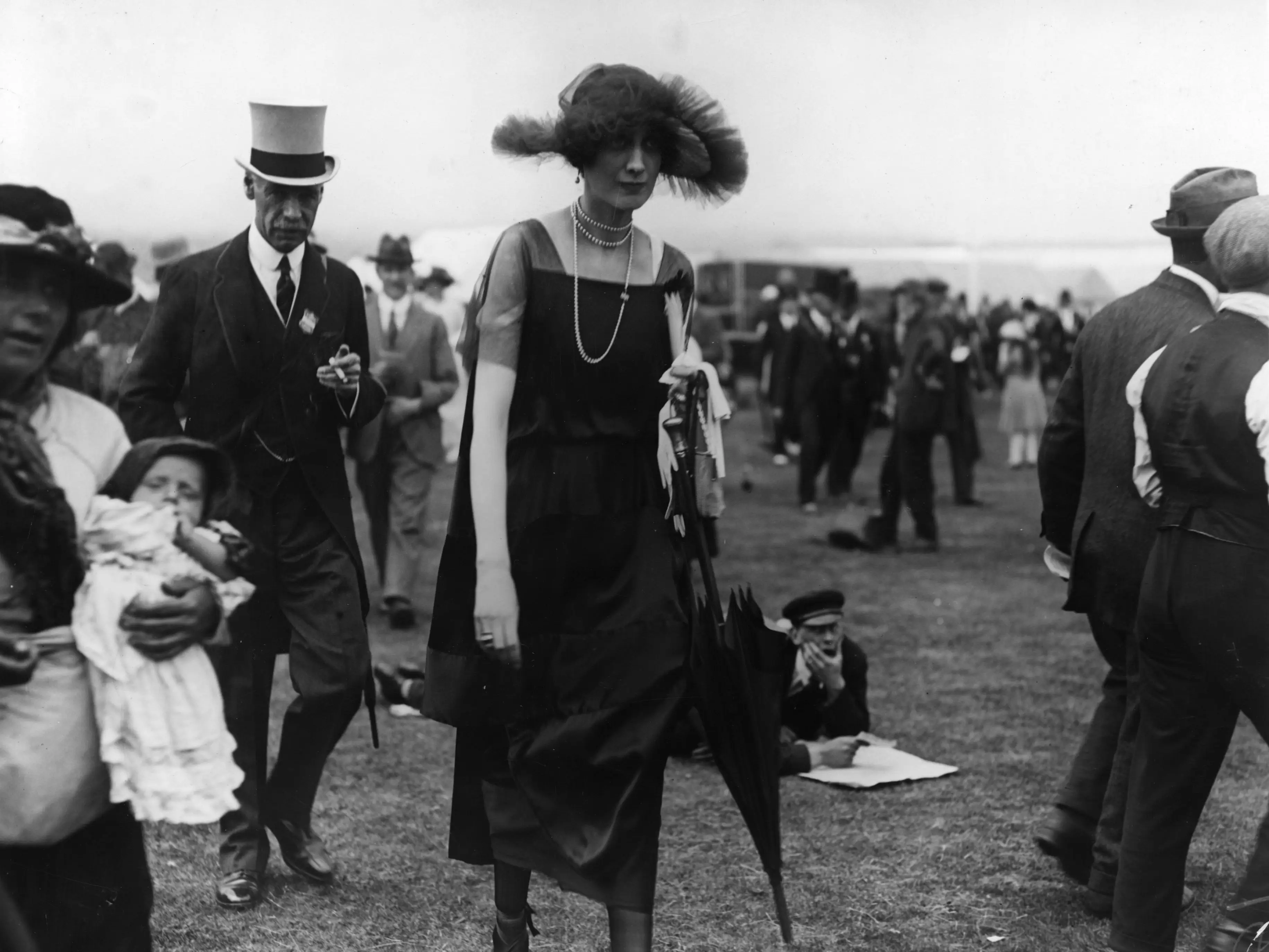 A woman at an Ascot horse race wore a loose, short-sleeve dress, a long necklace, and a ruffled, wide-brimmed hat.