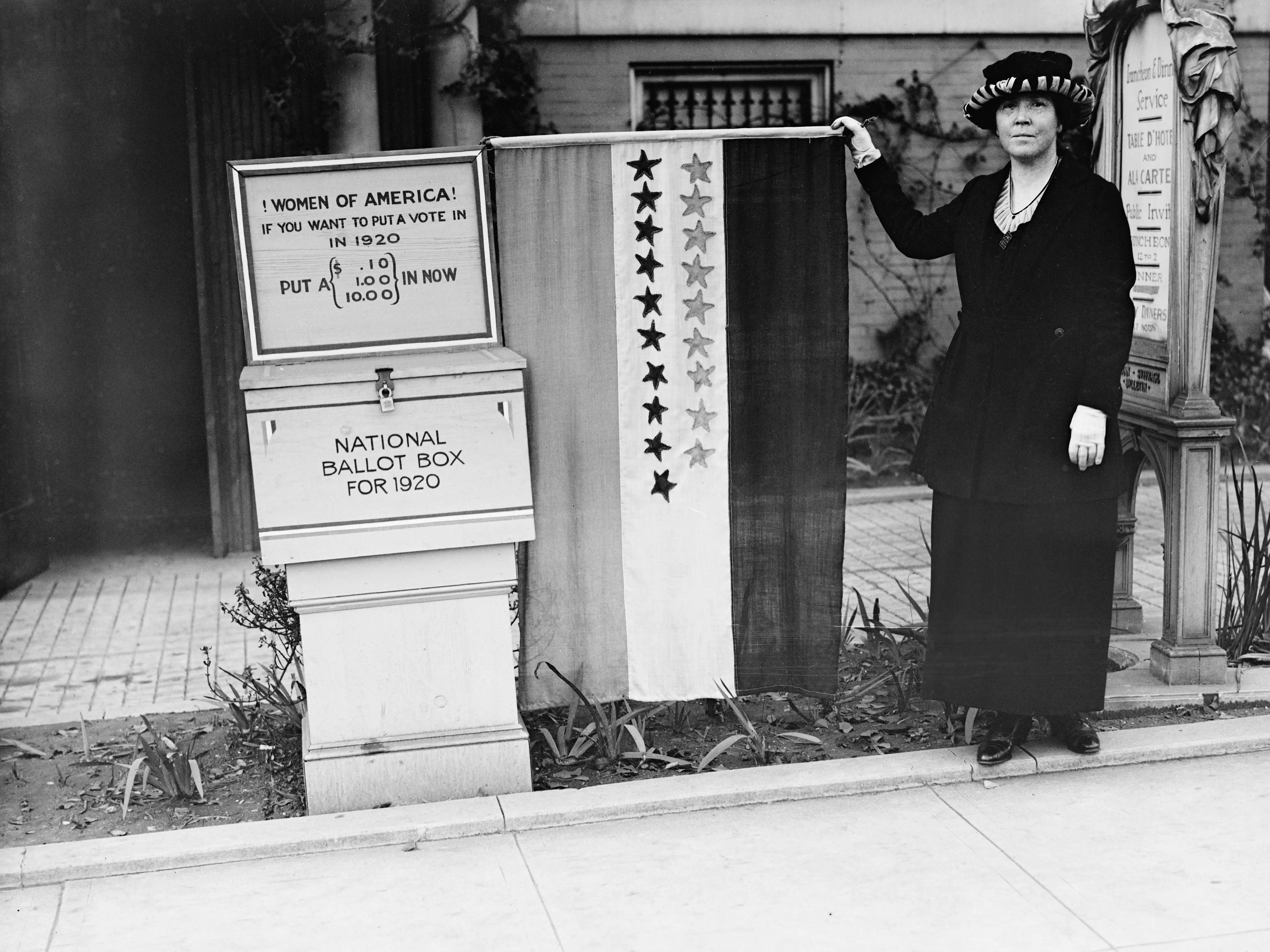 A suffragette standing next to a National Ballot Box in 1920. Above the ballot box is a sign that reads, 