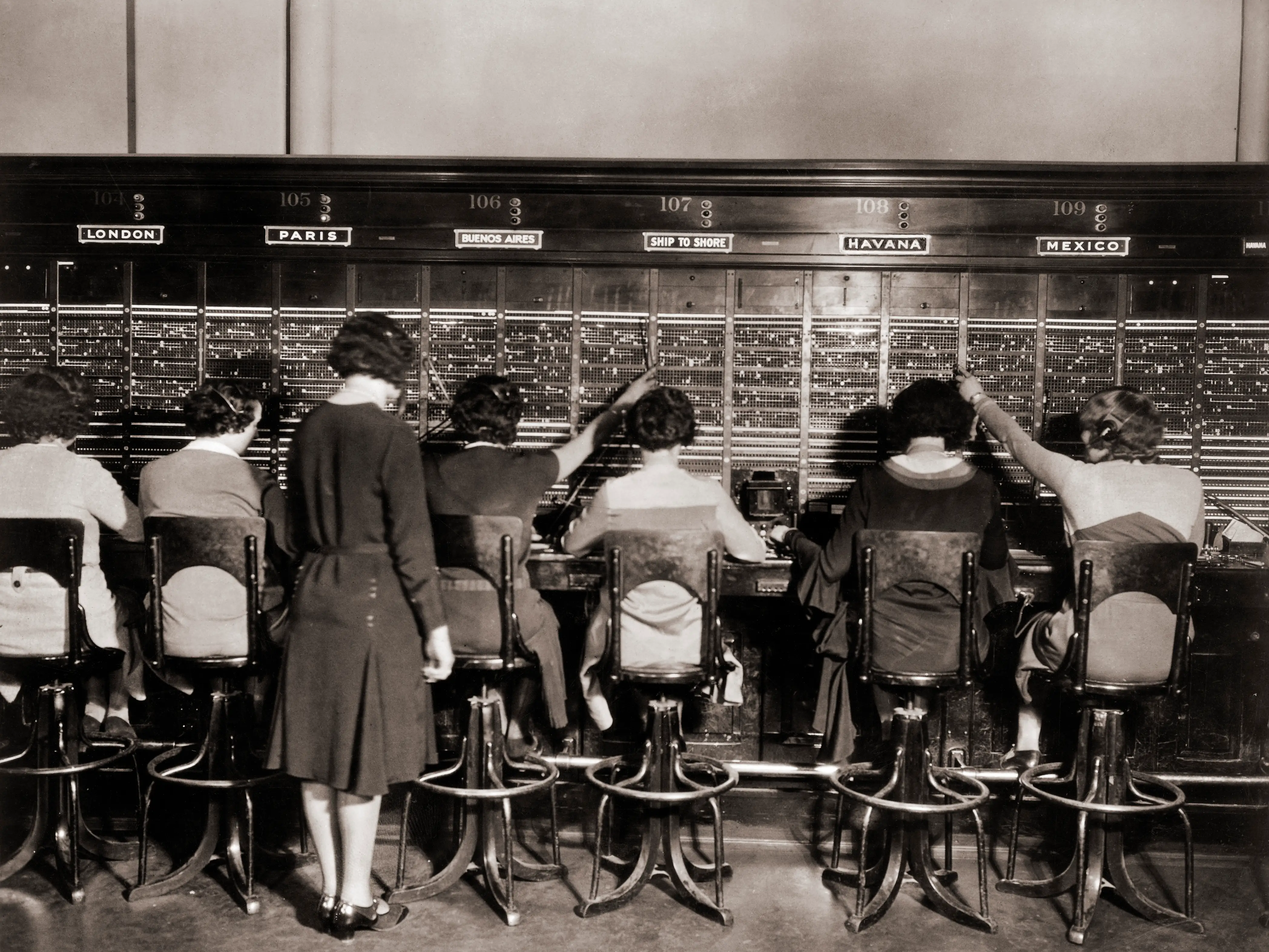 A group of women operating a switchboard in 1925. Another woman stands behind them, watching.