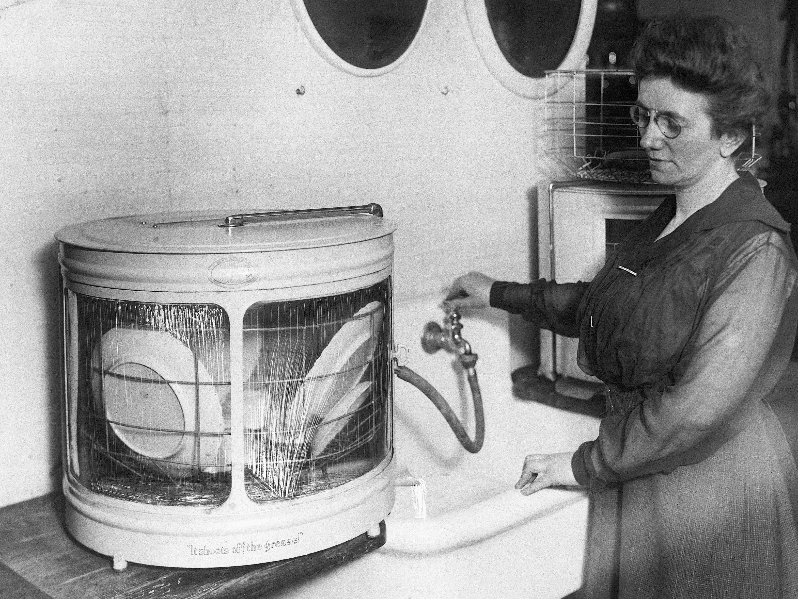 A woman demonstrating how to use one of the earliest dishwashers.