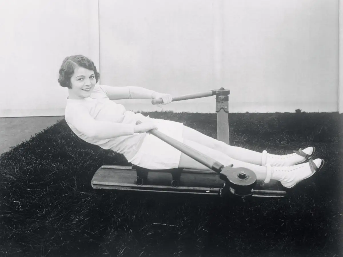 Helen Chadwick smiling and using a 1920s rowing machine.