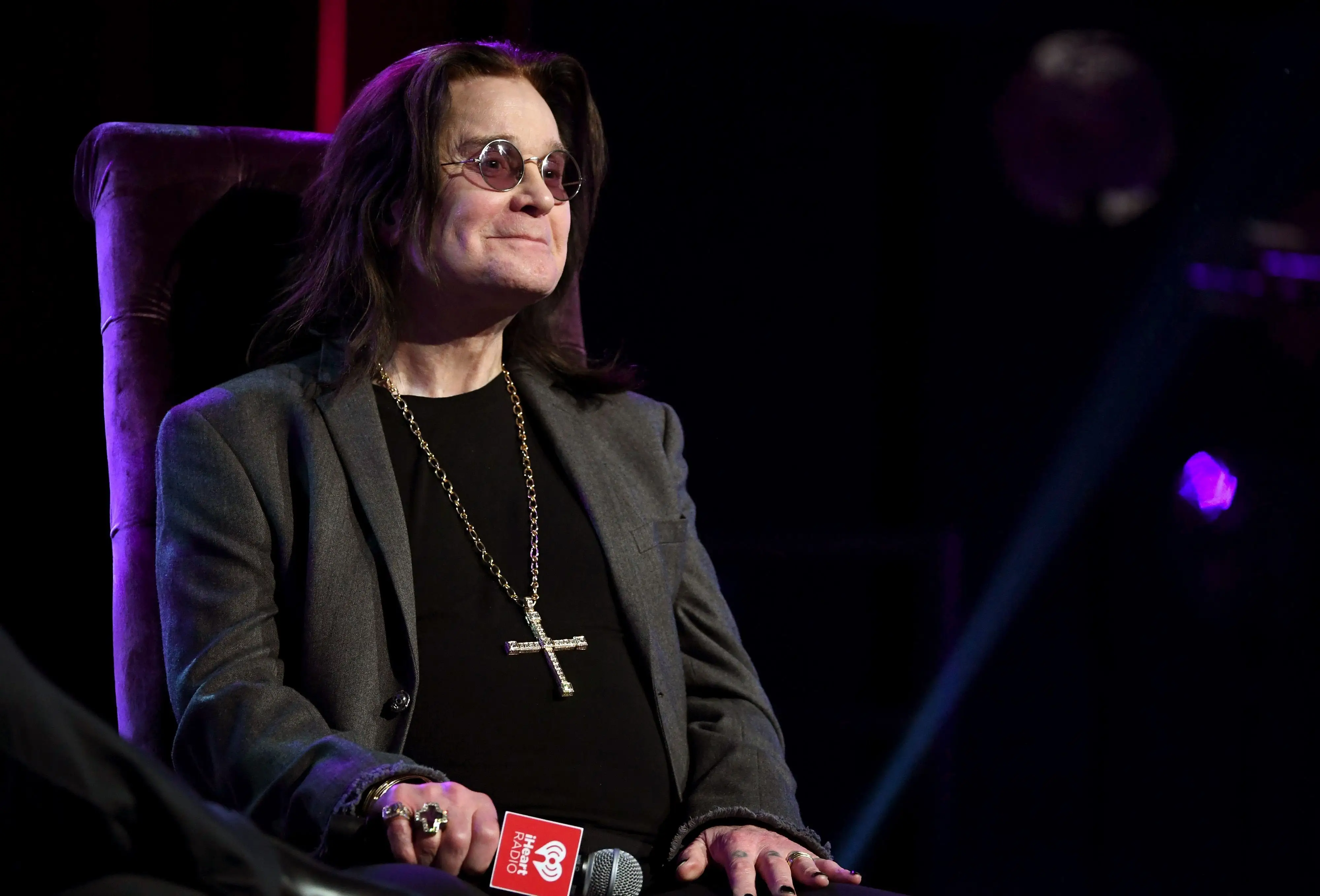 Ozzy Osbourne sitting onstage while holding a microphone.
