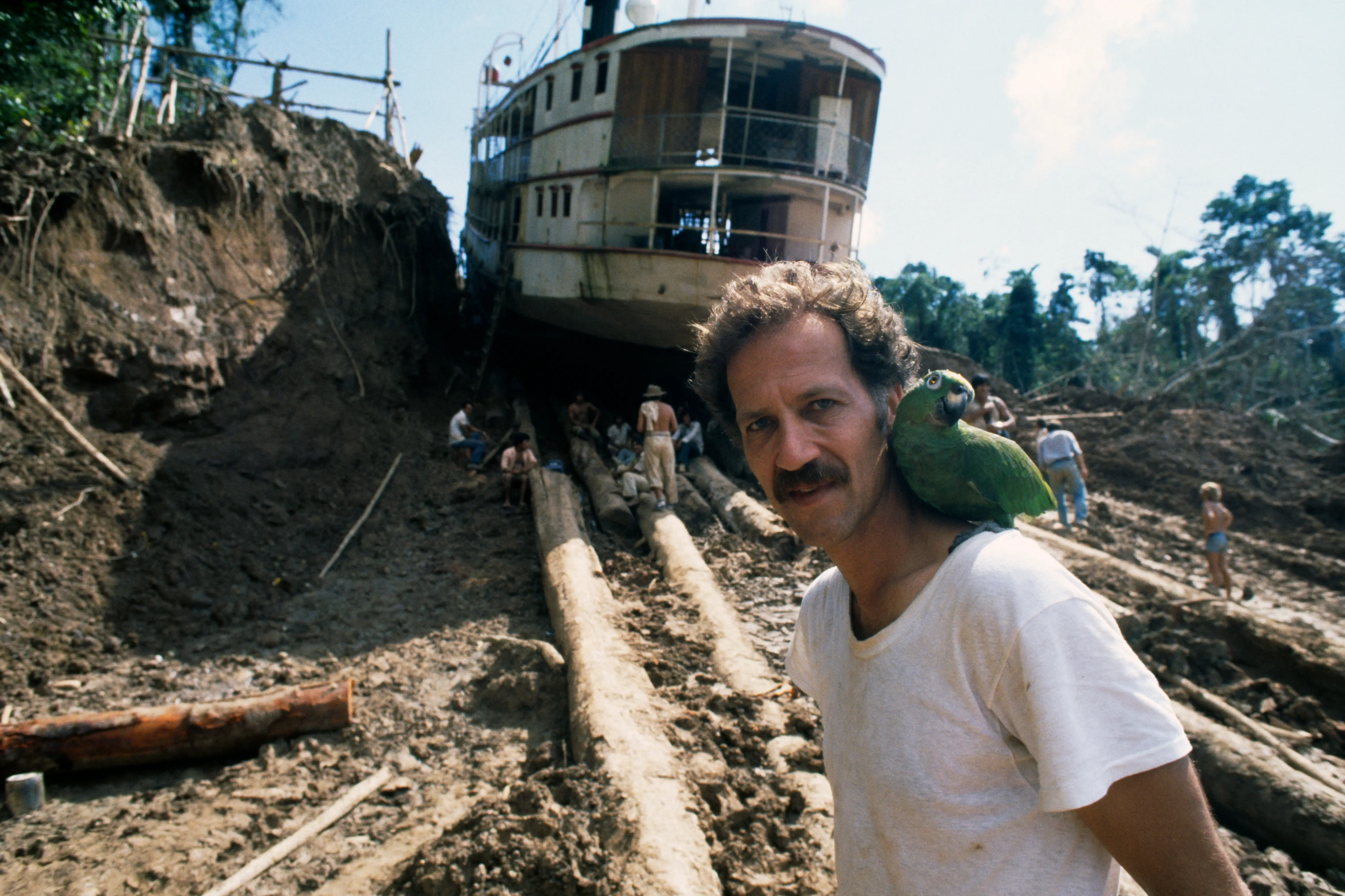 Werner Herzog with a bird on his shoulder in front of a ship being pulled up a hill