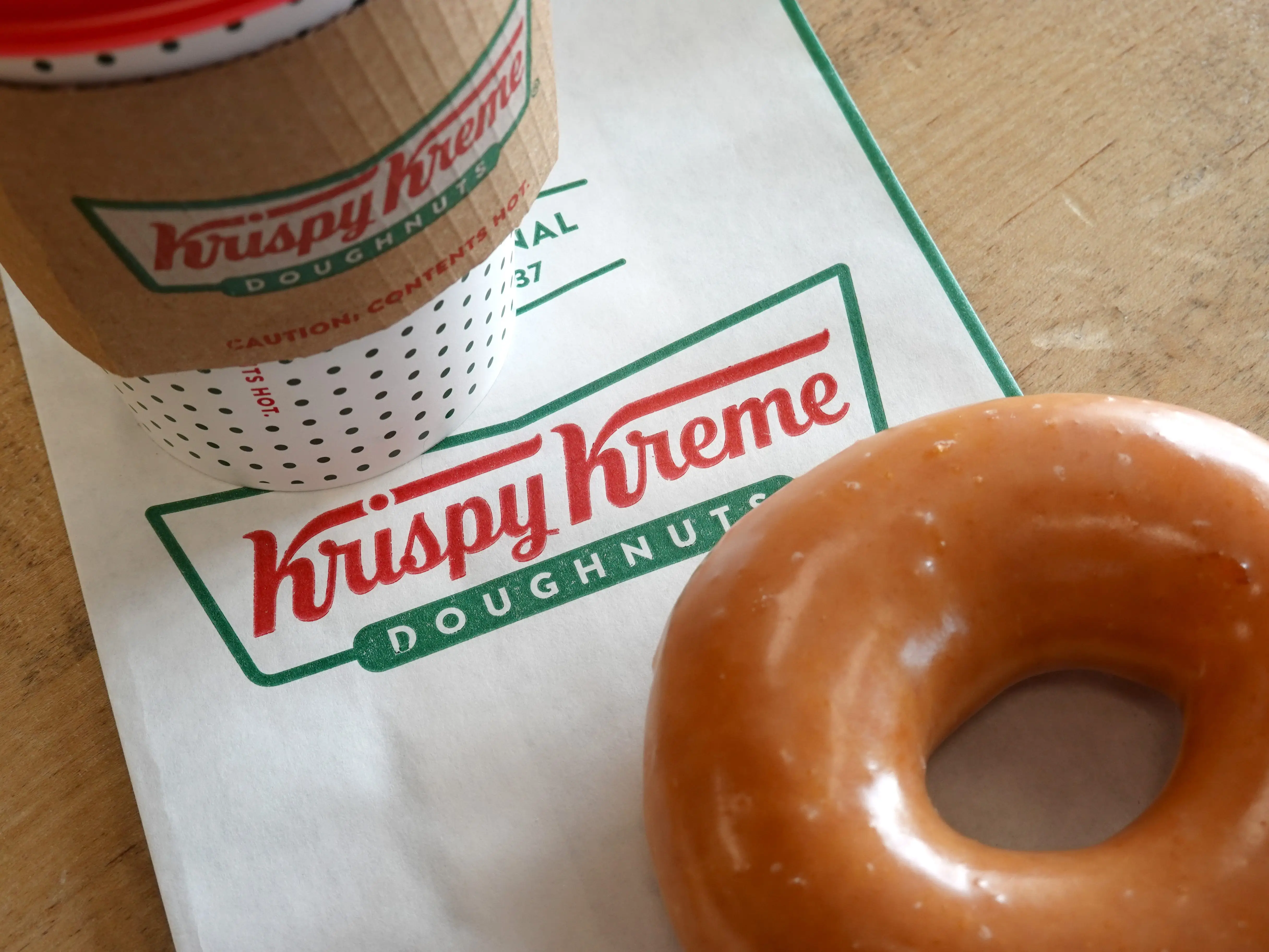Krispy Kreme glazed doughnut, bag, and coffee.
