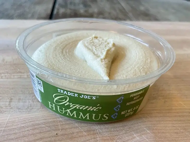 Container of Trader Joe's organic hummus, with a green label, and swirled top of hummus