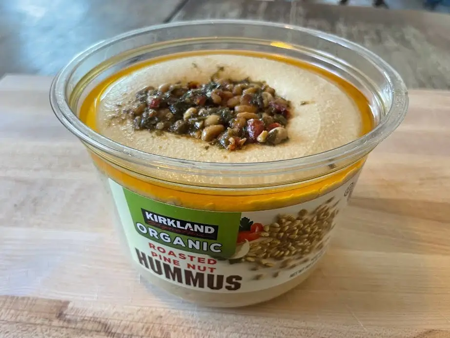 Container of Kirkland Signature organic roasted-pine-nut hummus with pile of pine nuts and oil on the top of the hummus