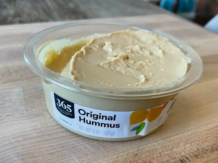 Container of Whole Foods 365 original hummus with a white label on a wooden container