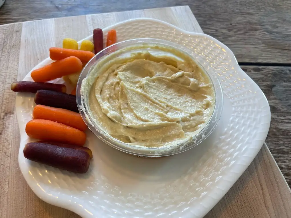 Stirred up container of Wegmans hummus on a white plate with multicolored carrots