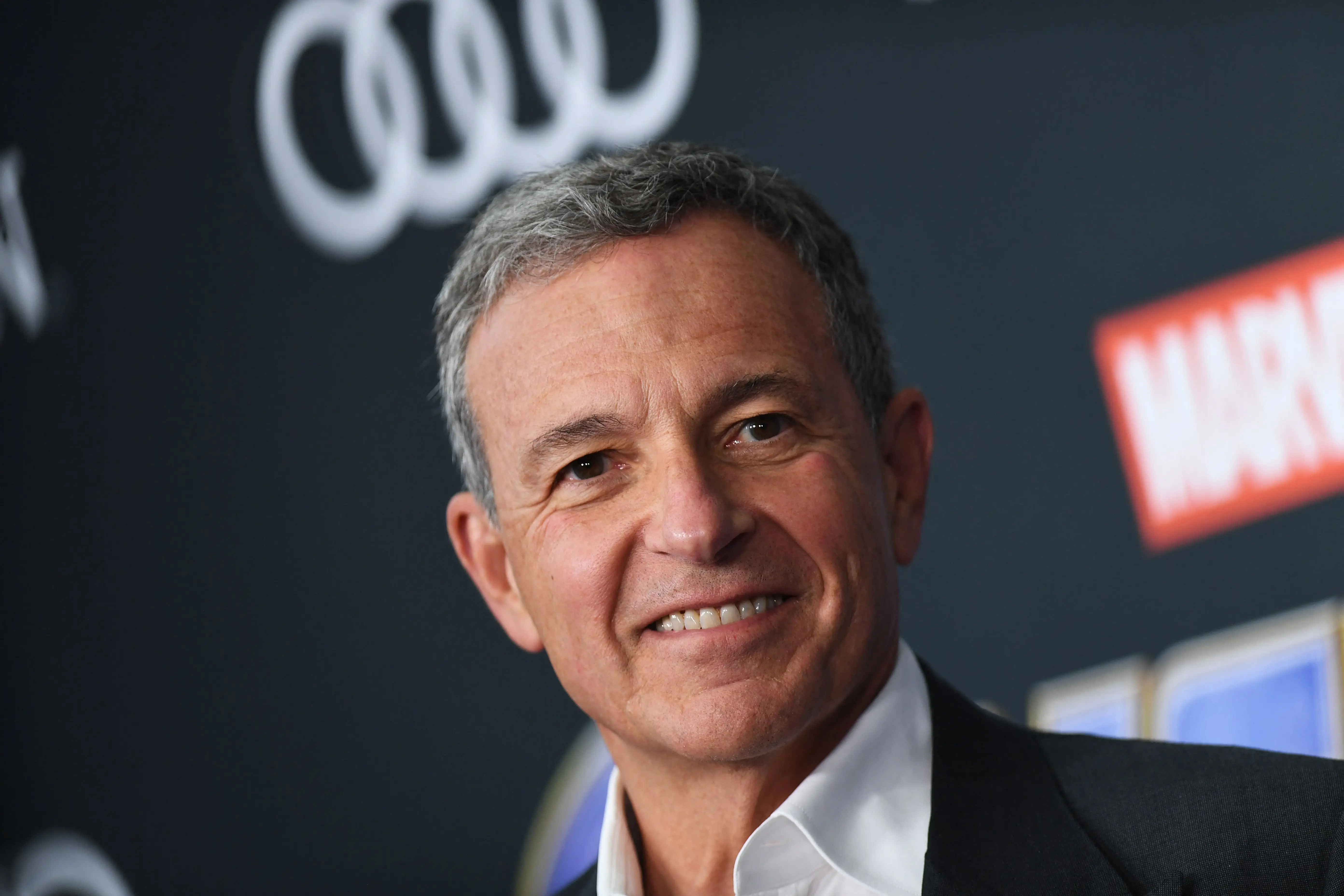 Bob Iger smiles at the camera in front of a Marvel logo