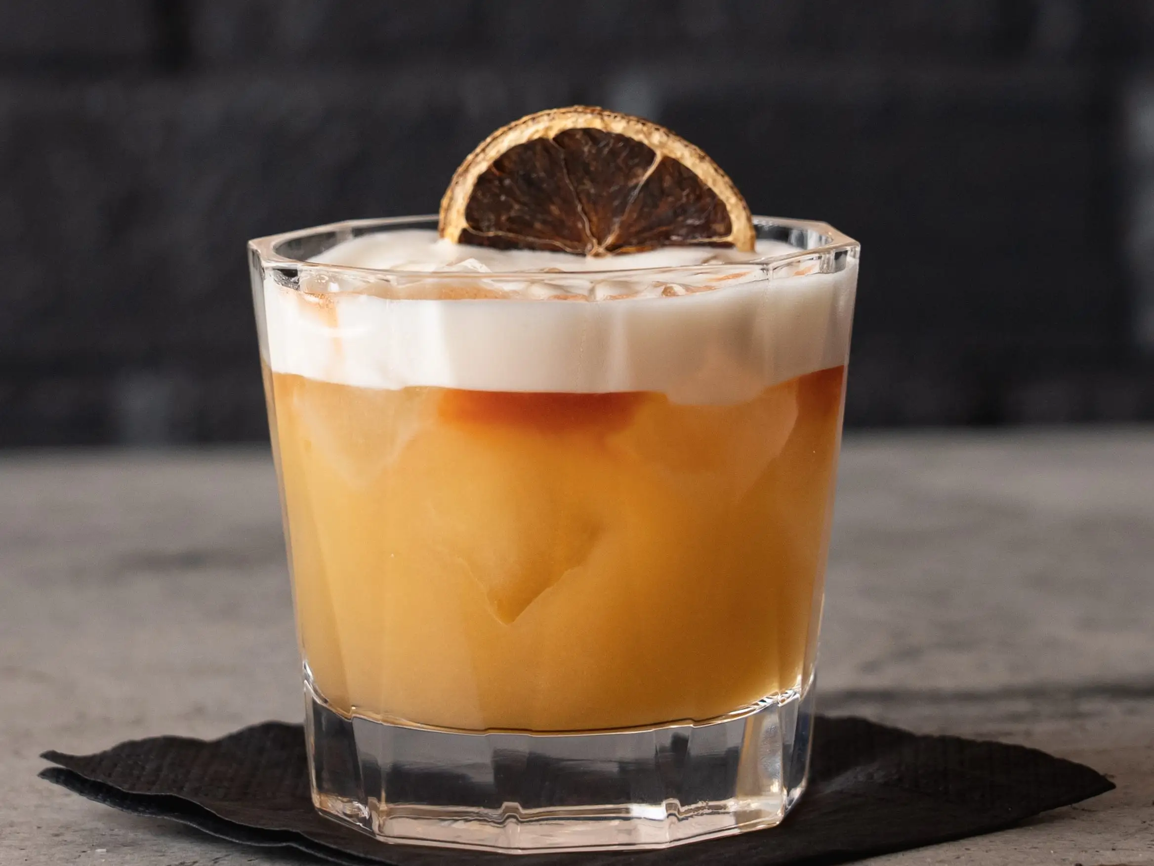amaretto sour cocktail with a dried orange slice on a cocktail napkin