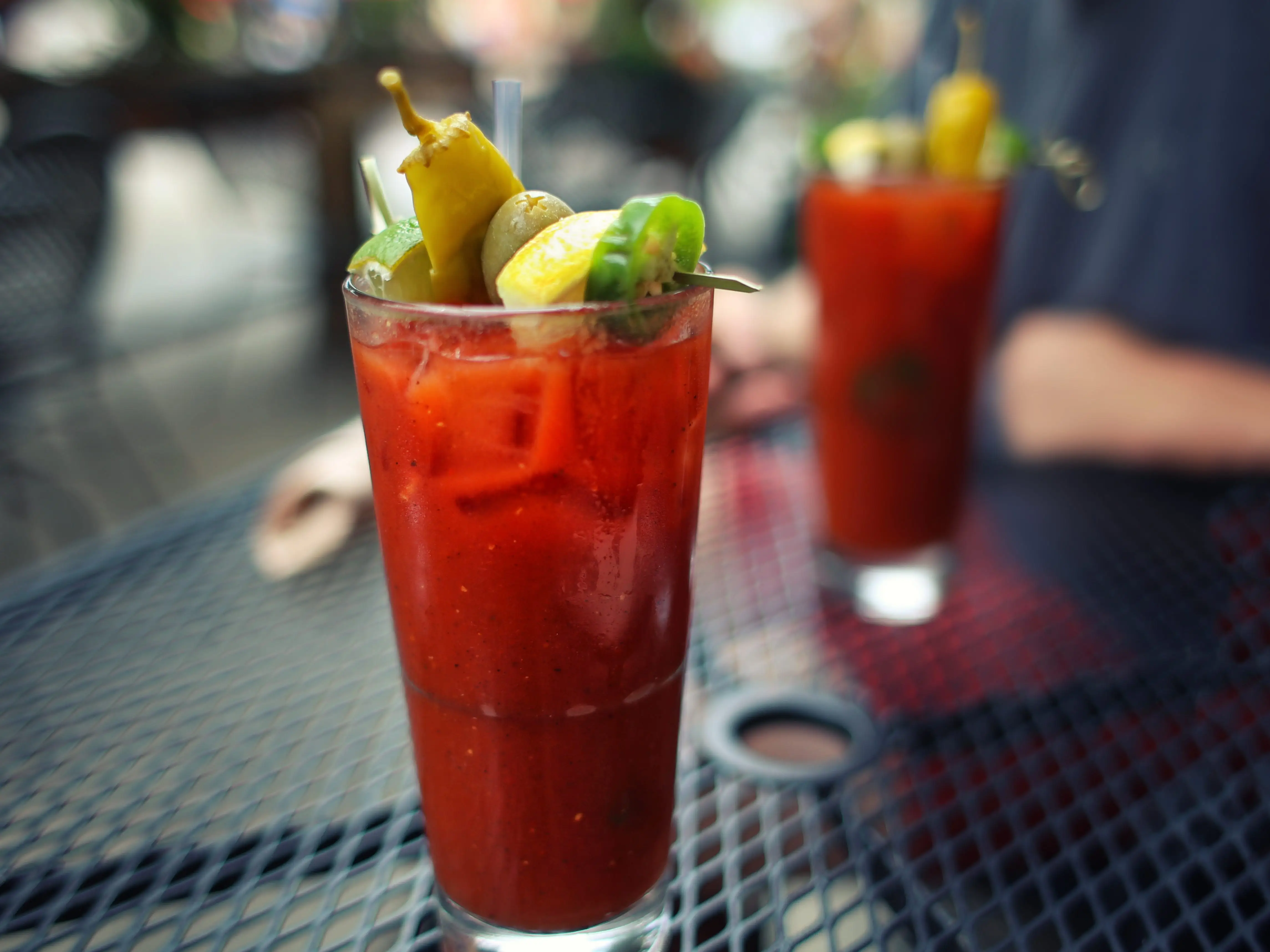 two garnished bloody mary cocktails on an outdoor table
