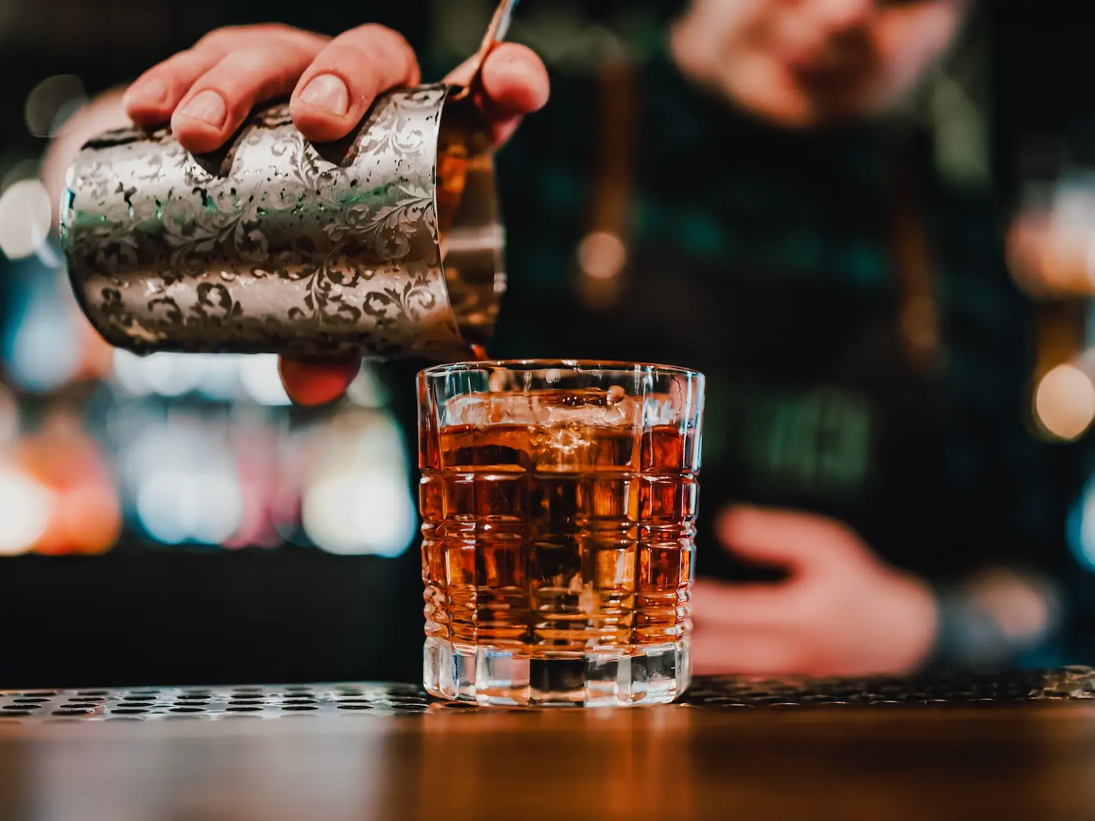 bartender pouring a simple cocktail into a short glass on a bar