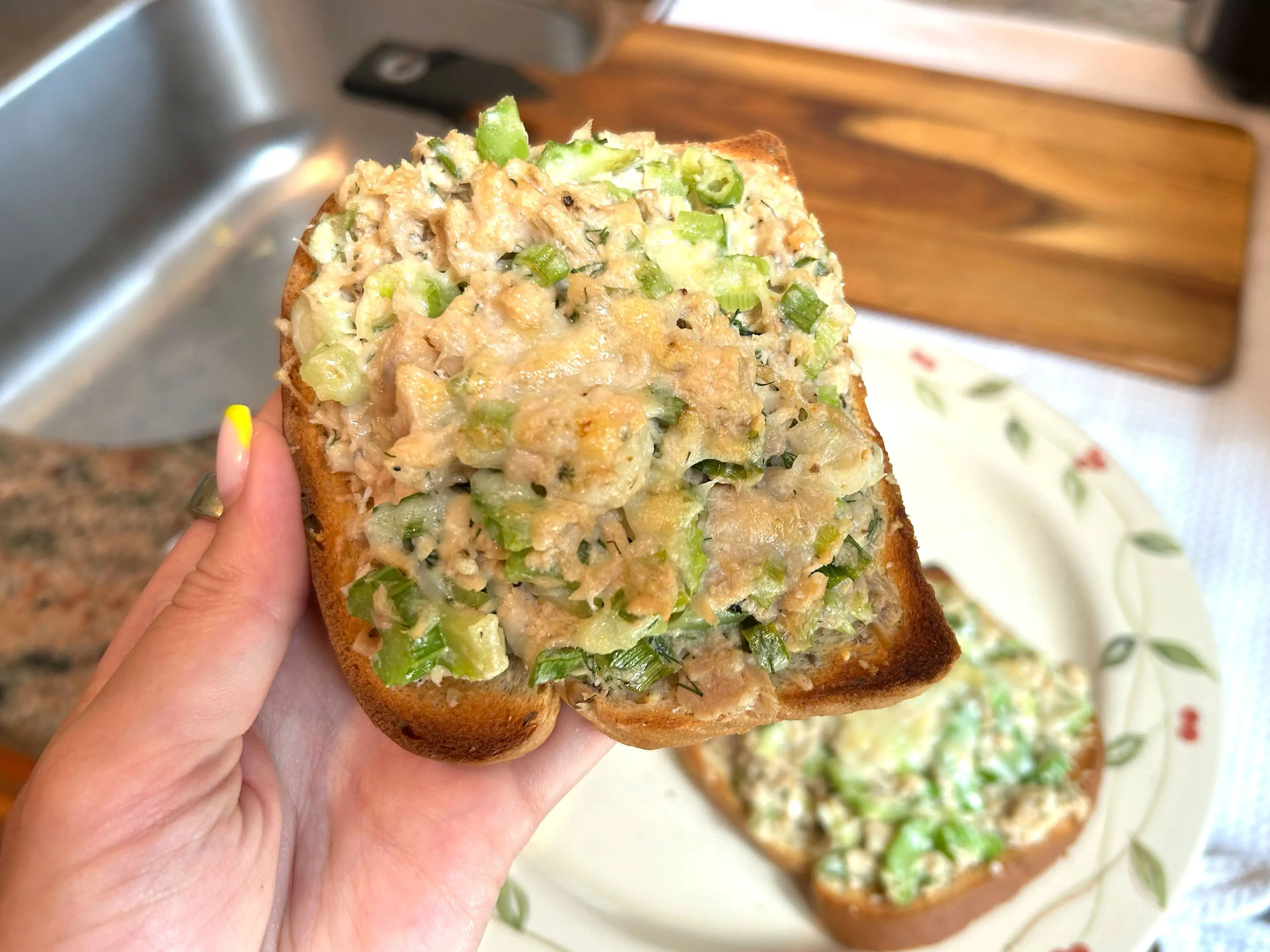 Lara holding up a slice of tuna melt over a plate.