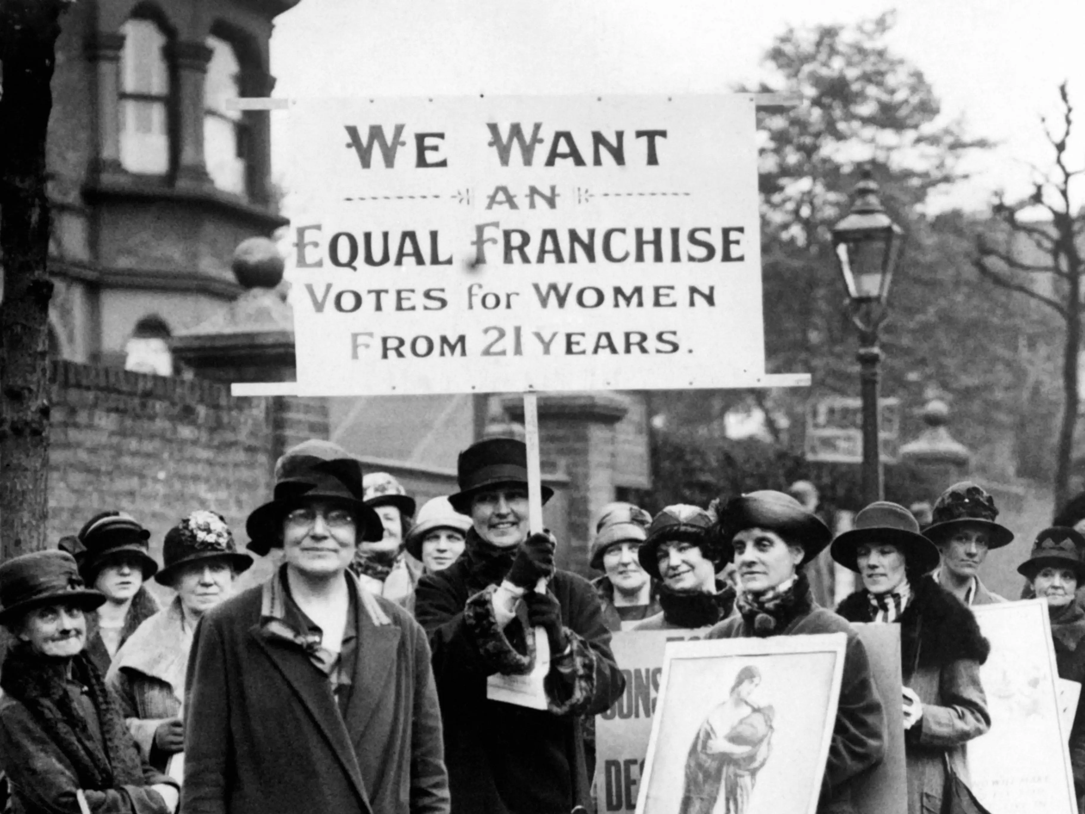 Labour Party Vice President Susan Lawrence, left, in front of a group of women protesting for the right to vote in London. Another woman holds a large sign that reads, 