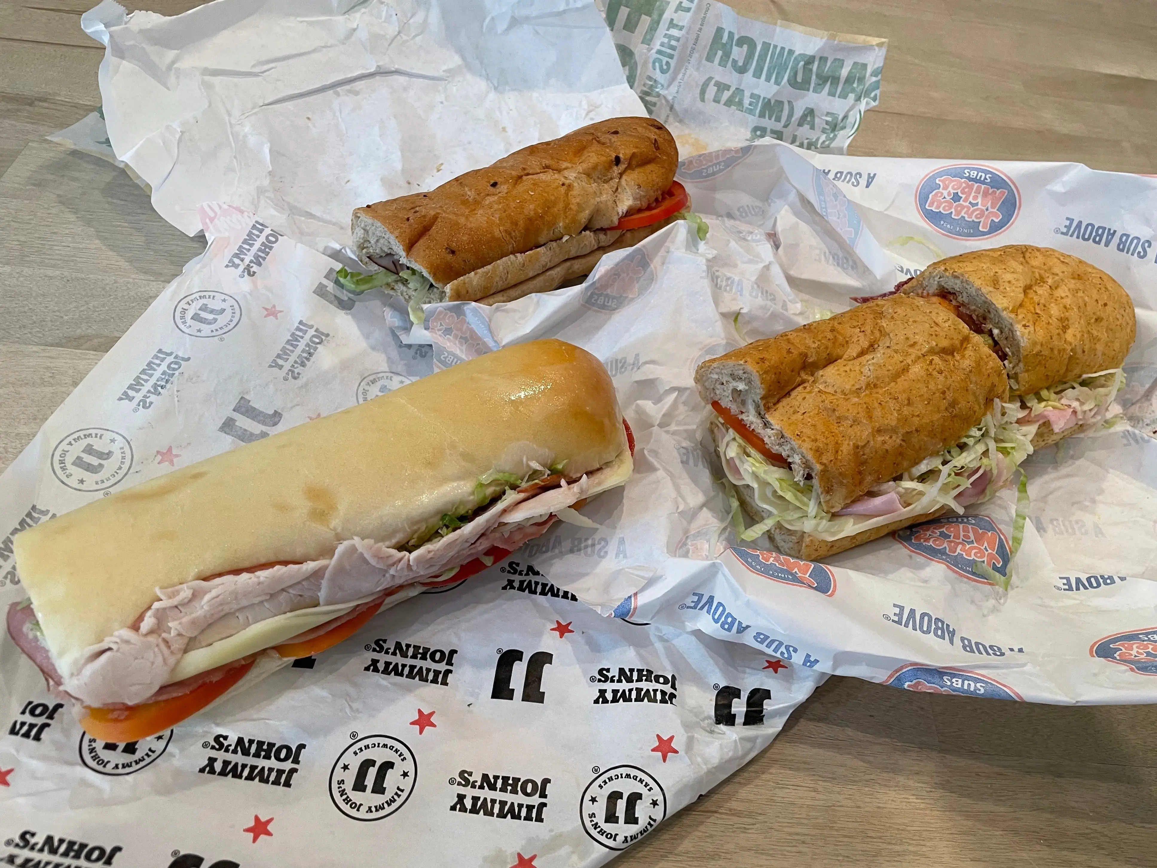 Three club sandwiches from Jimmy John's, Subway, and Jersey Mike's on a table.