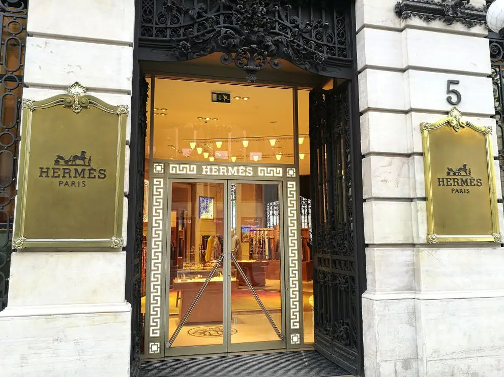Exterior of an Hermes store with a gold design on the door and gold plaques on the storefront next to the door