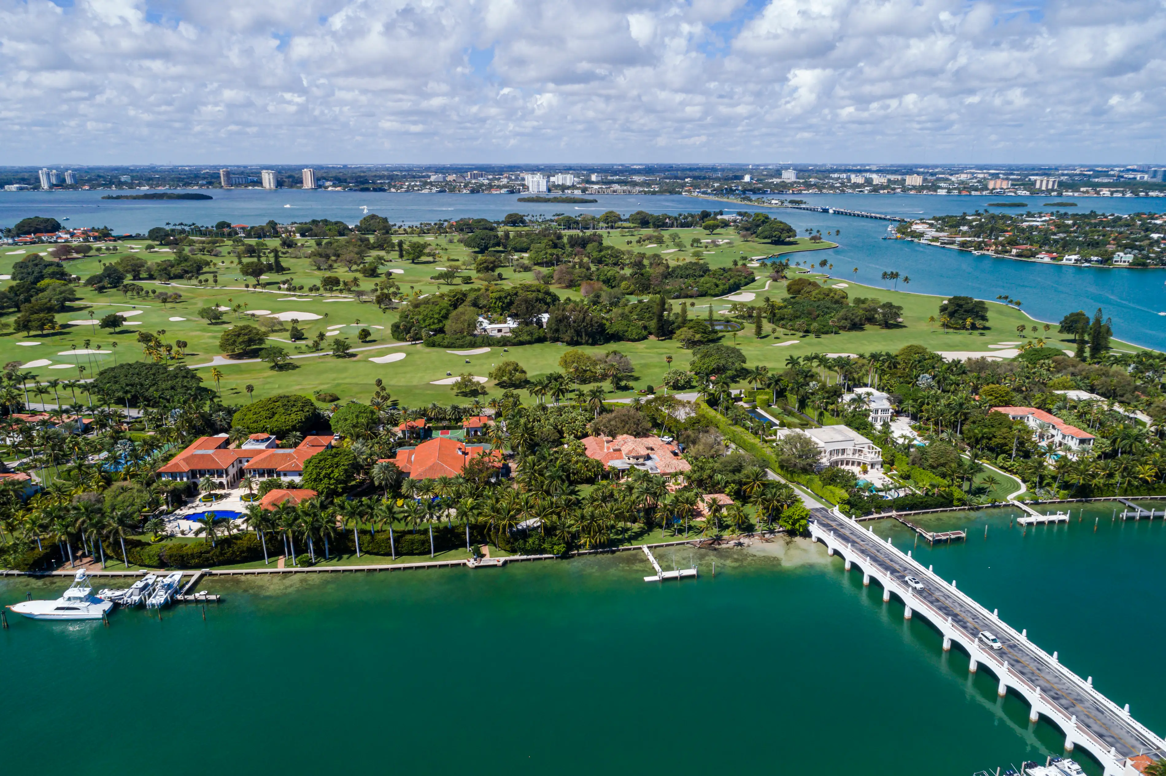 An aerial view of Indian Creek Island in Miami showing the bridge leading to it, some mansions, its golf course, and the blue water surrounding it