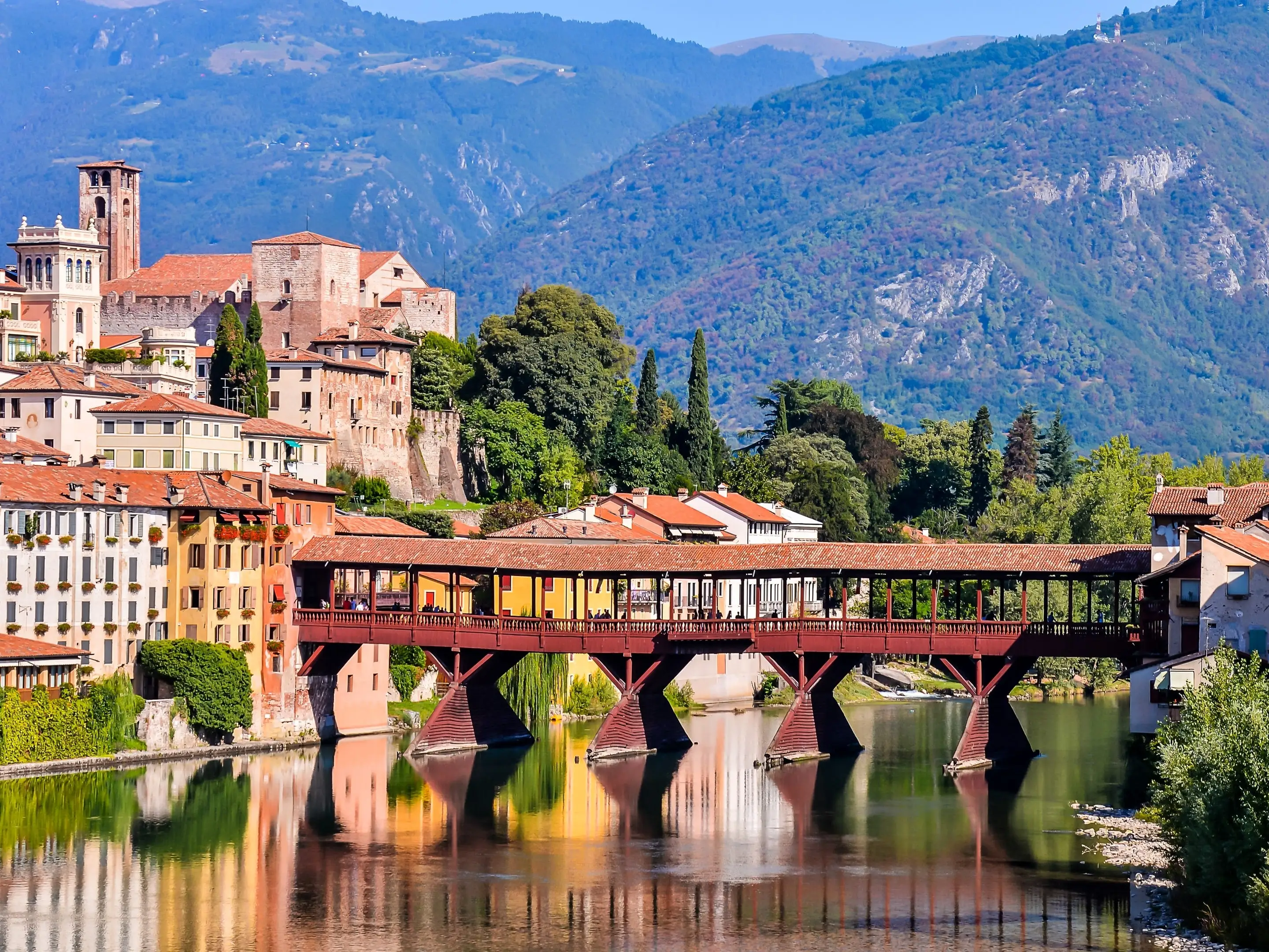 Colorful buildings and a covered bridge over a river in front of mountains.