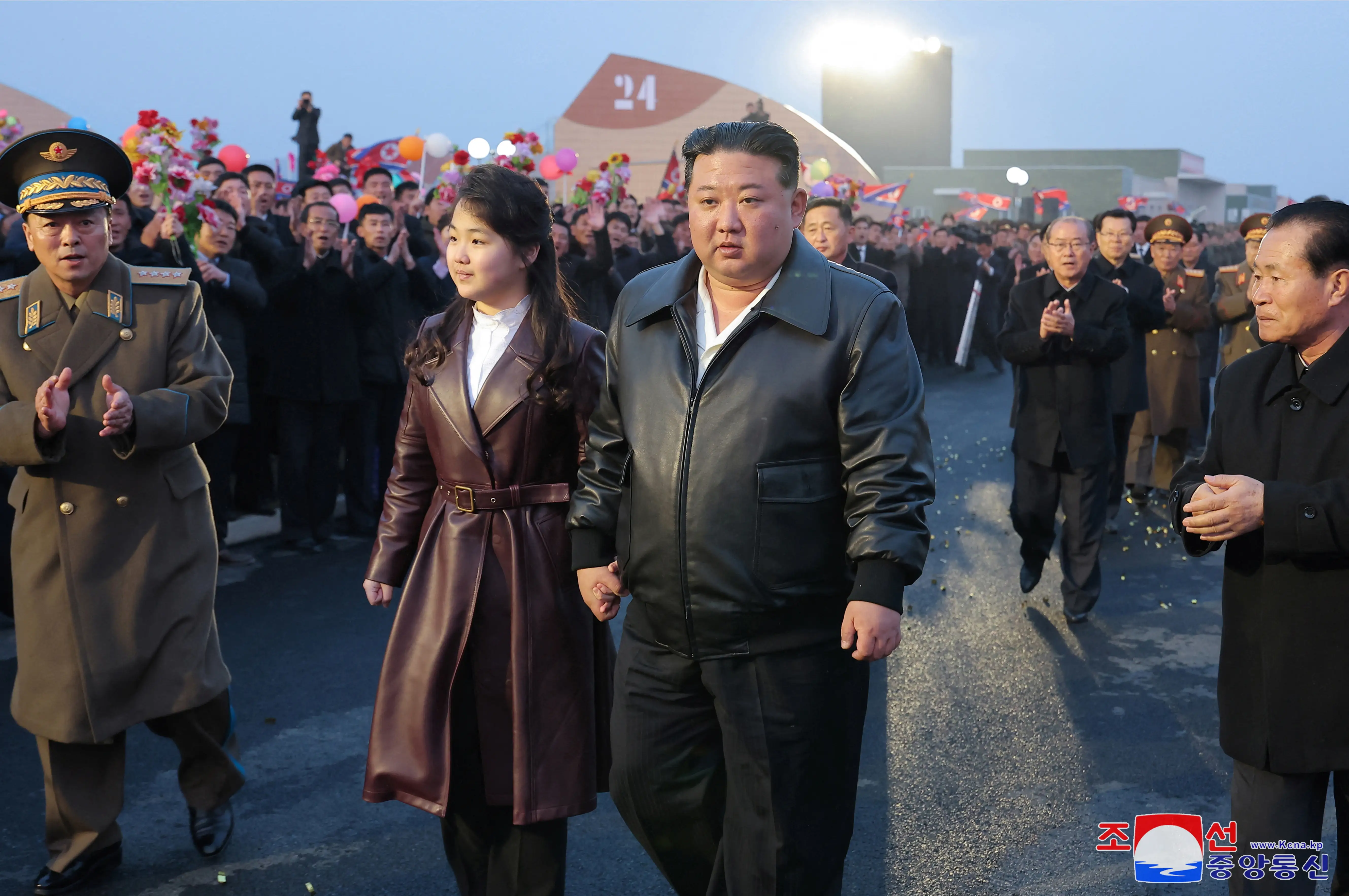 Kim Jong Un and Kim Ju Ae walk through a crowd, both weaing leather jackets