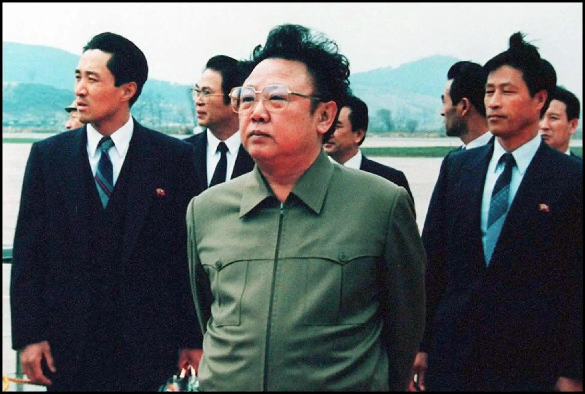 Kim Jong Il in a green collard suit in front of several men in suits