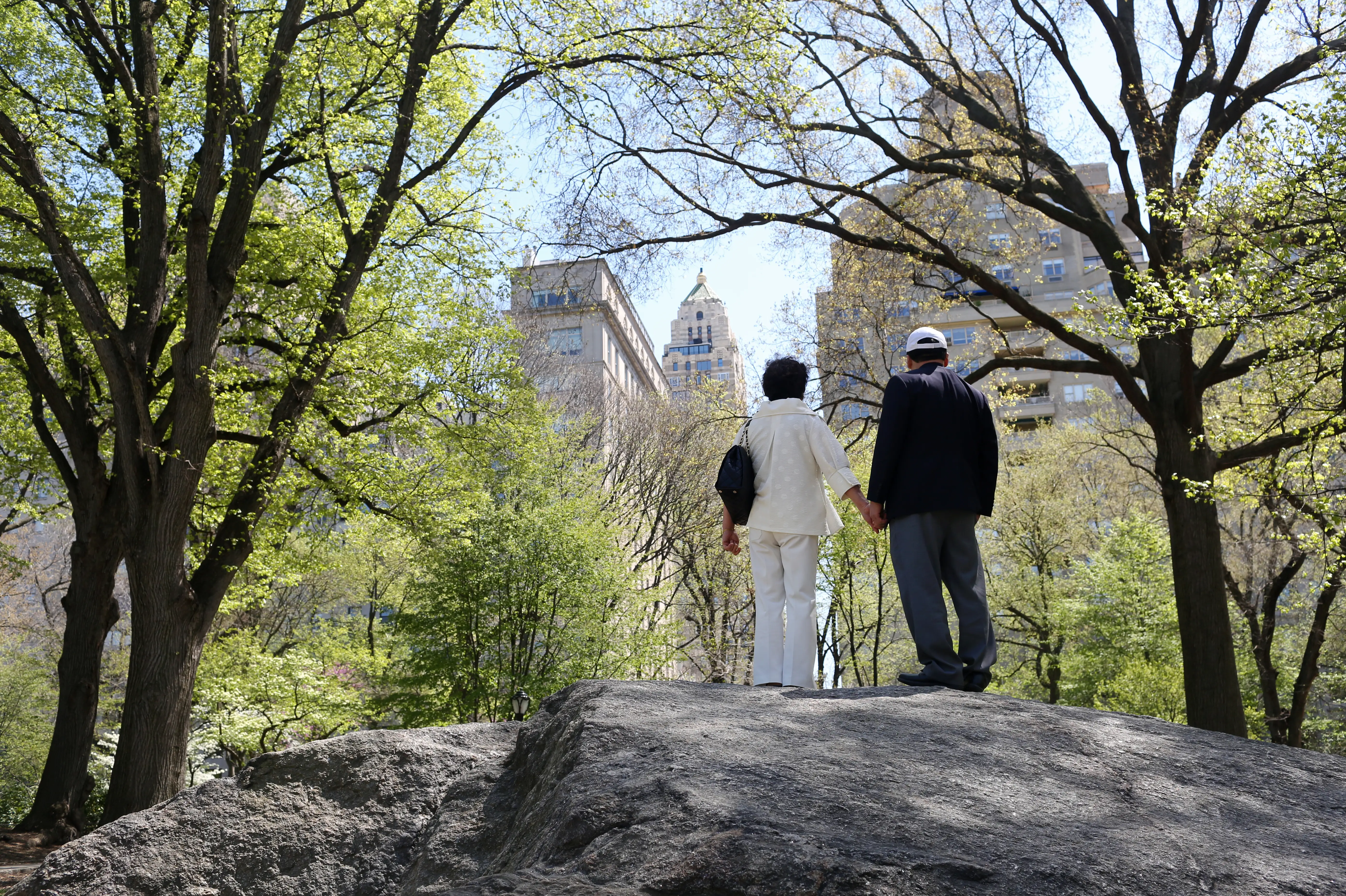 Ko Yong Suk wearing white pants and a cream top and Ri Gang in black and white hat in a park