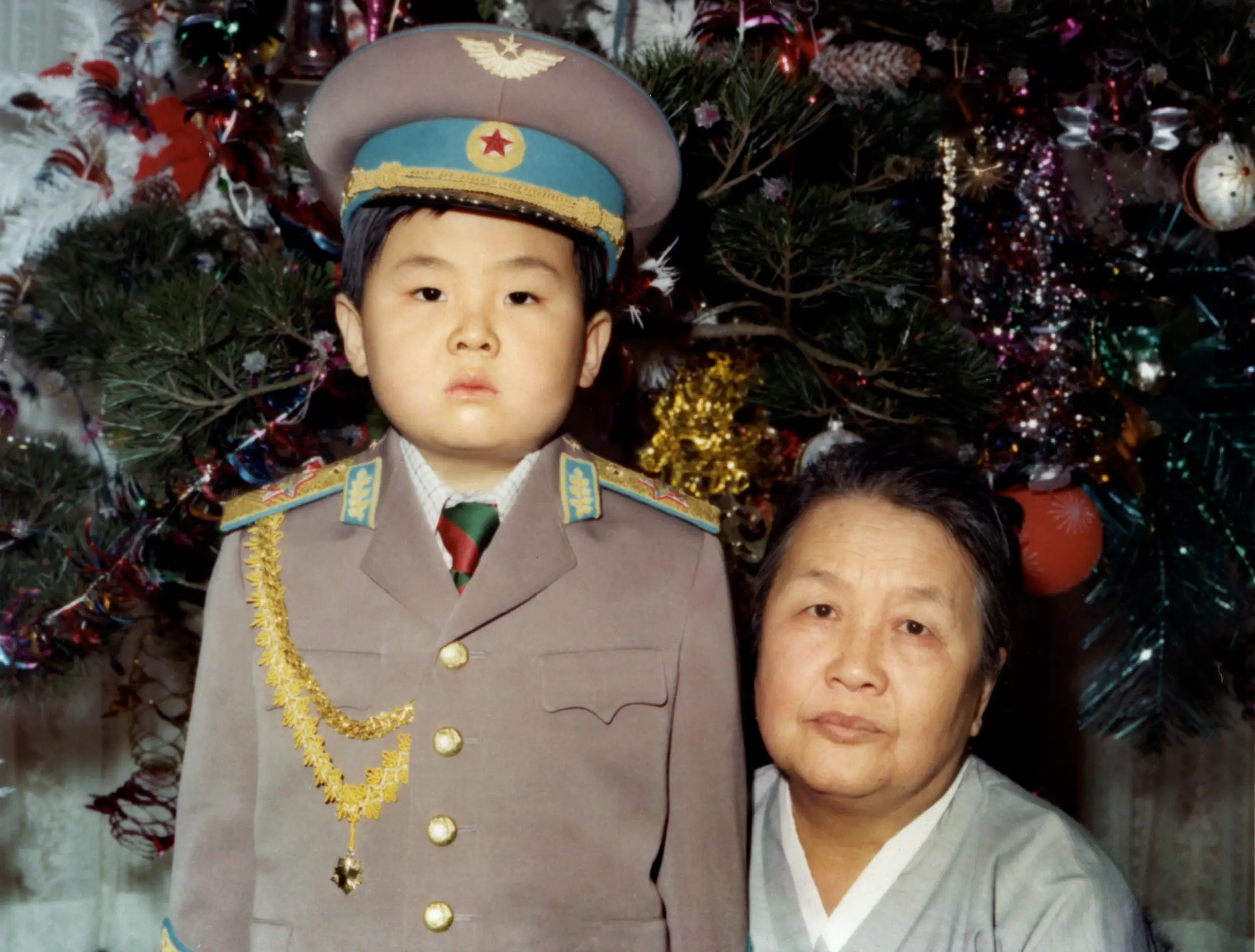 Kim Jong Nam as a boy dressed in military uniform next to his grandmother in front of a decorated Christmas tree