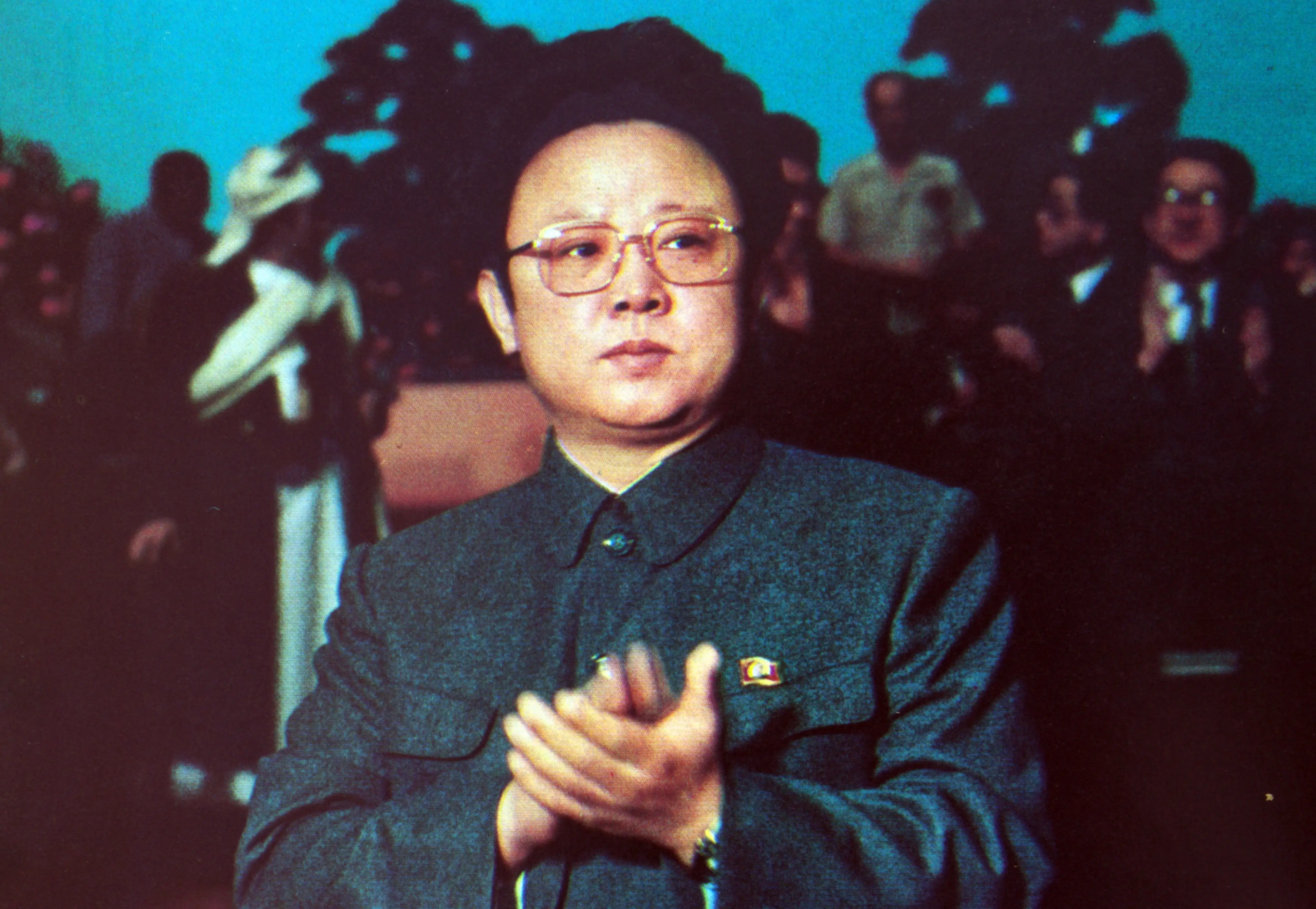 Kim Jong Il wearing glasses and a gray coat clapping