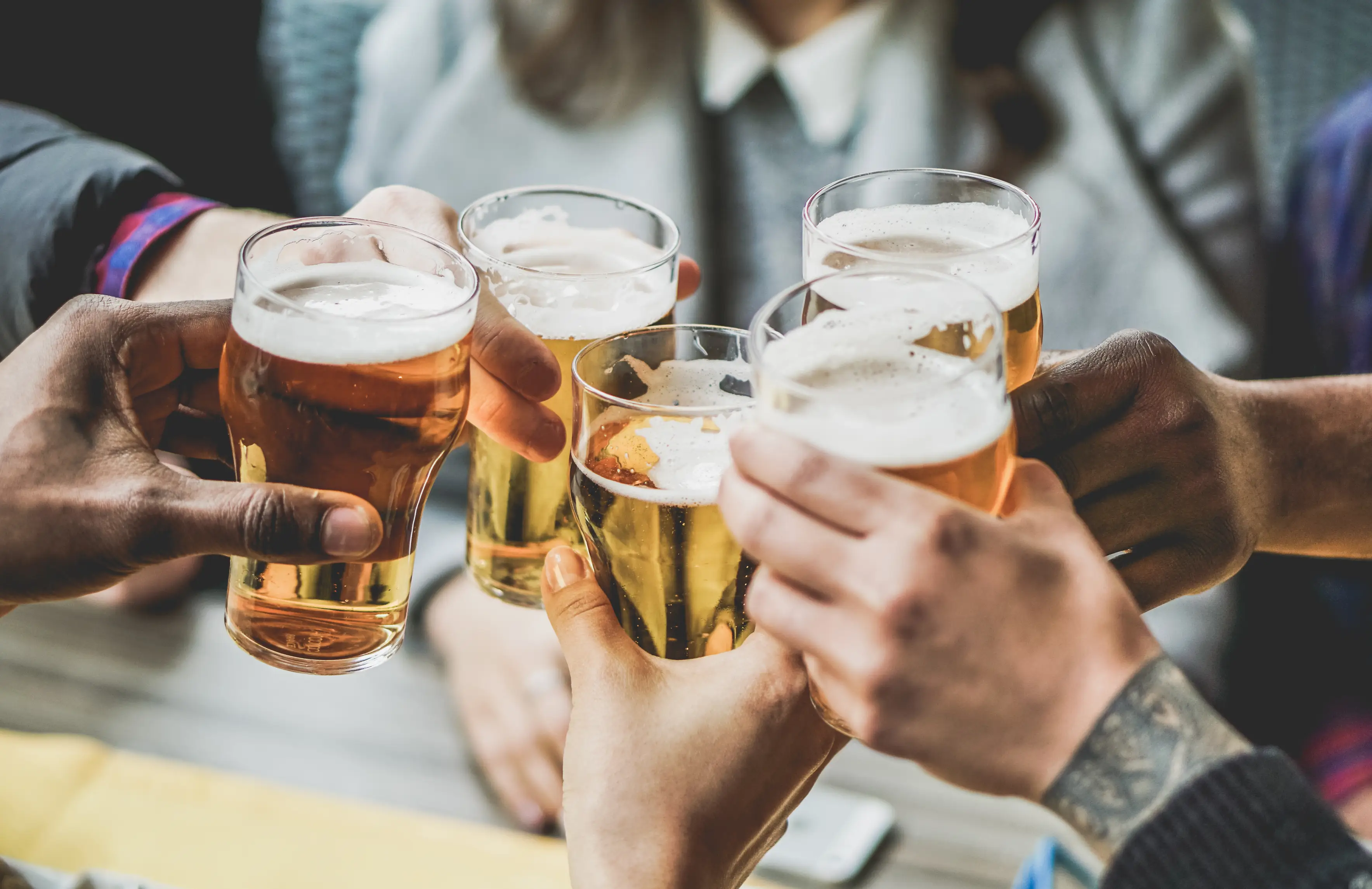 A close-up of people's hands holding pints of beer and cheersing.