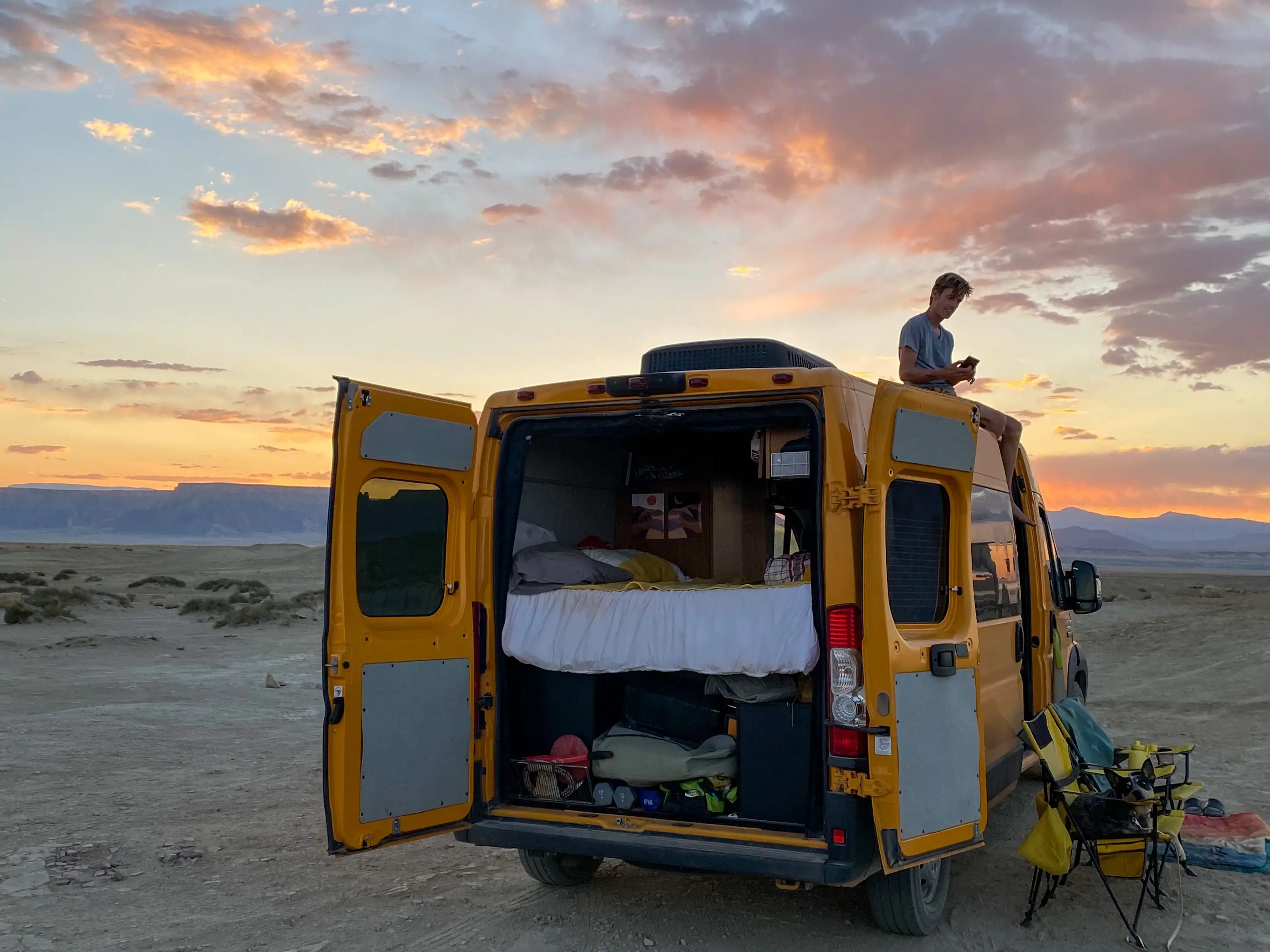 The author's van with the back doors open to reveal the bed and storage as the sun sets.
