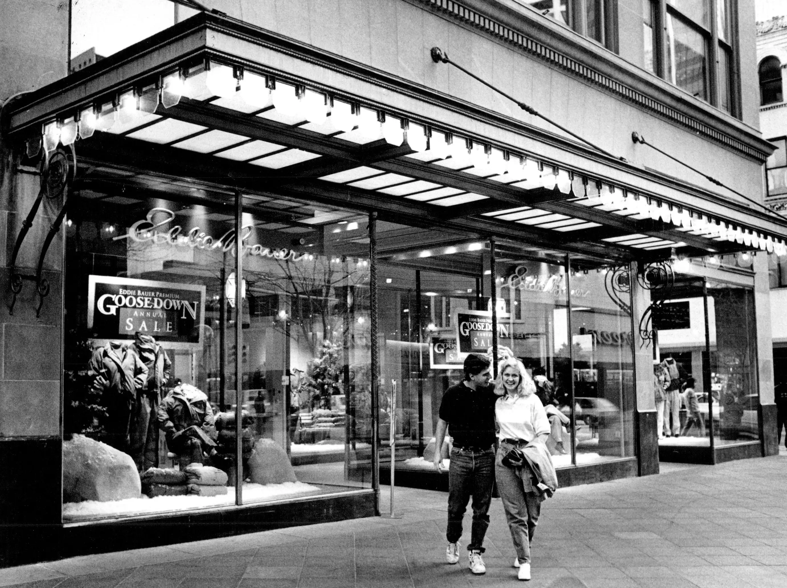 Black and white photo showing two people in front of an Eddie Bauer store.