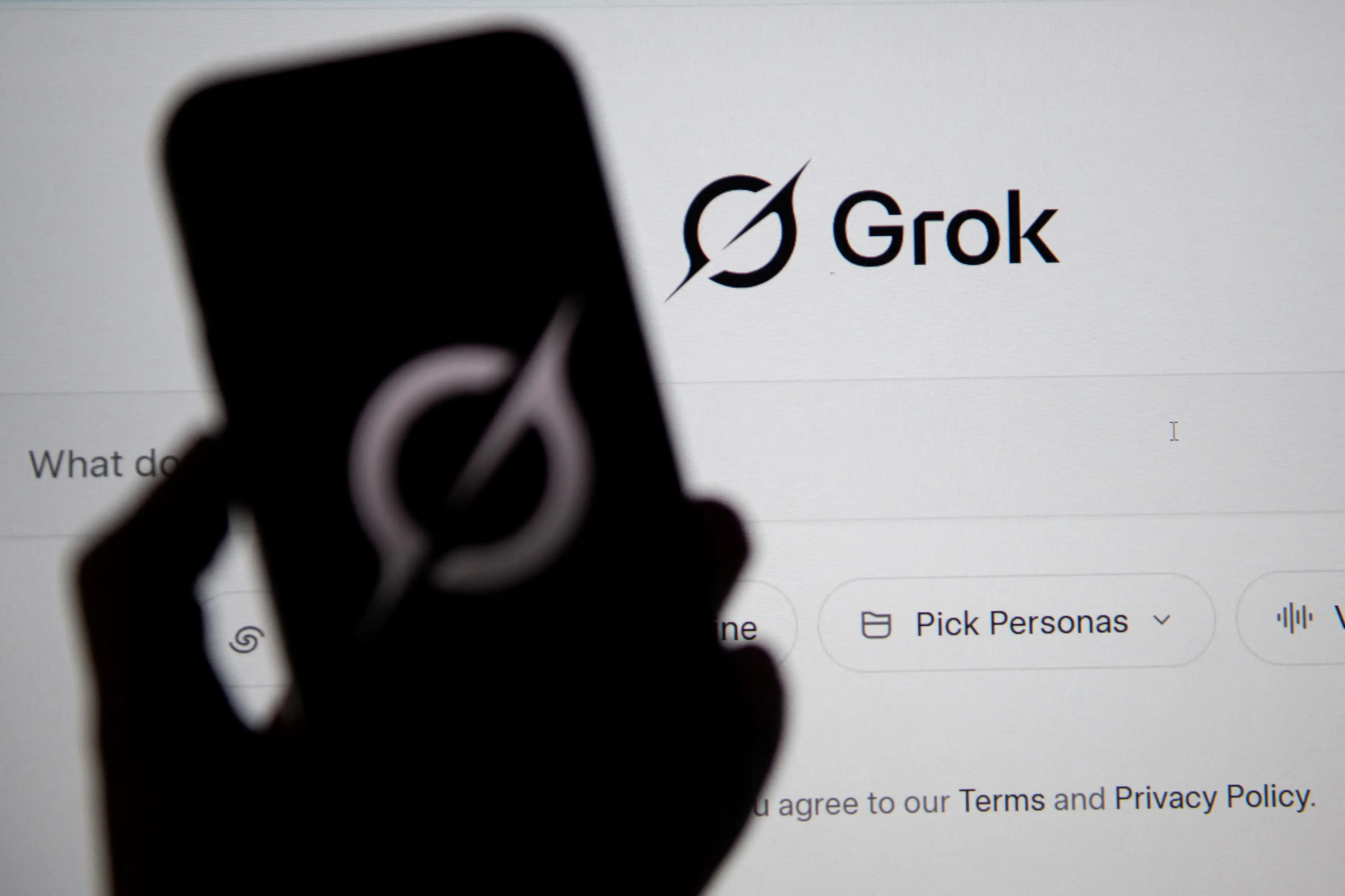 Grok website is seen on a computer screen next to a mobile phone displaying the logo in Bogota on February 12, 2026.