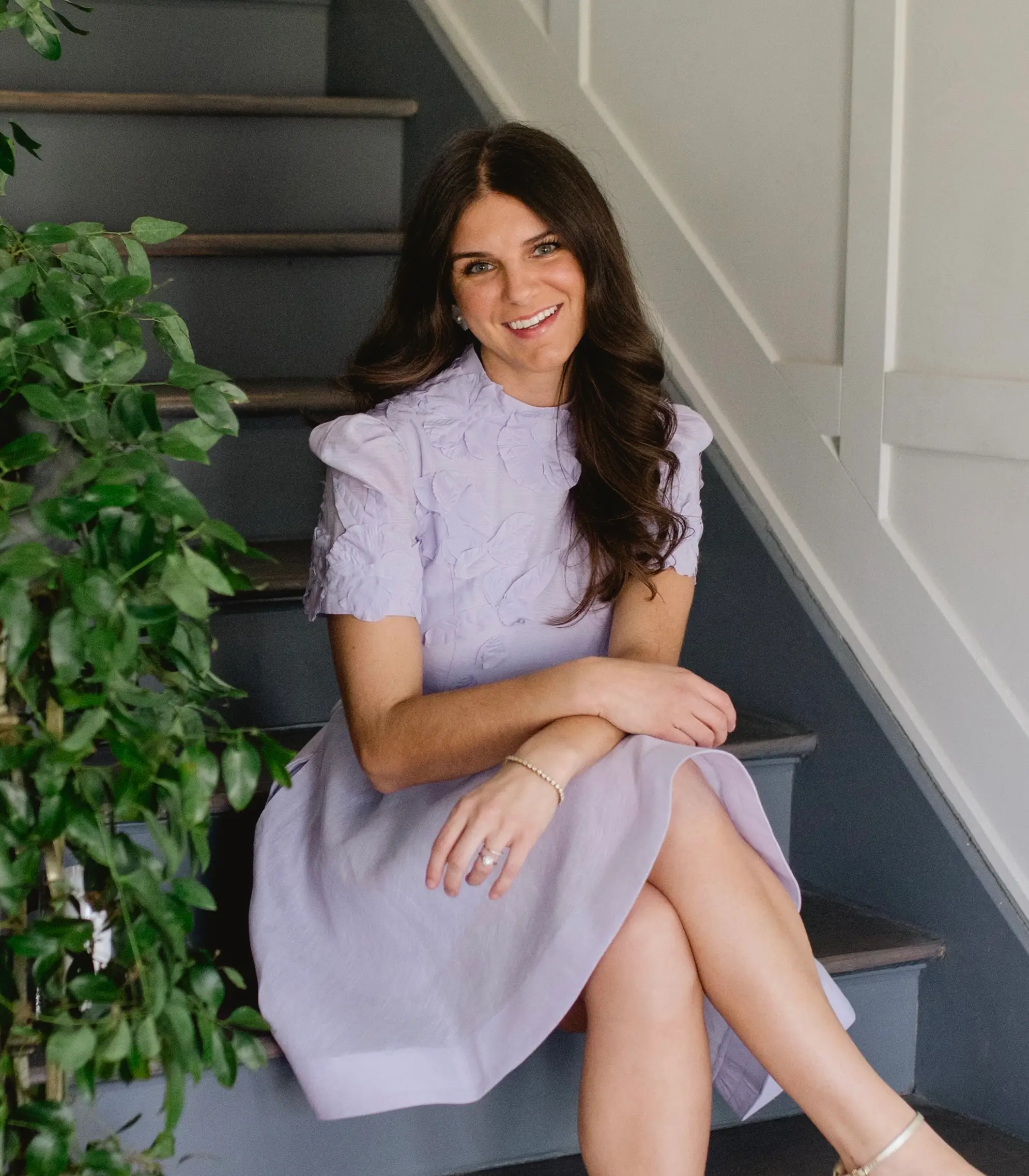 A woman in a purple dress sits on a blue staircase and smiles.