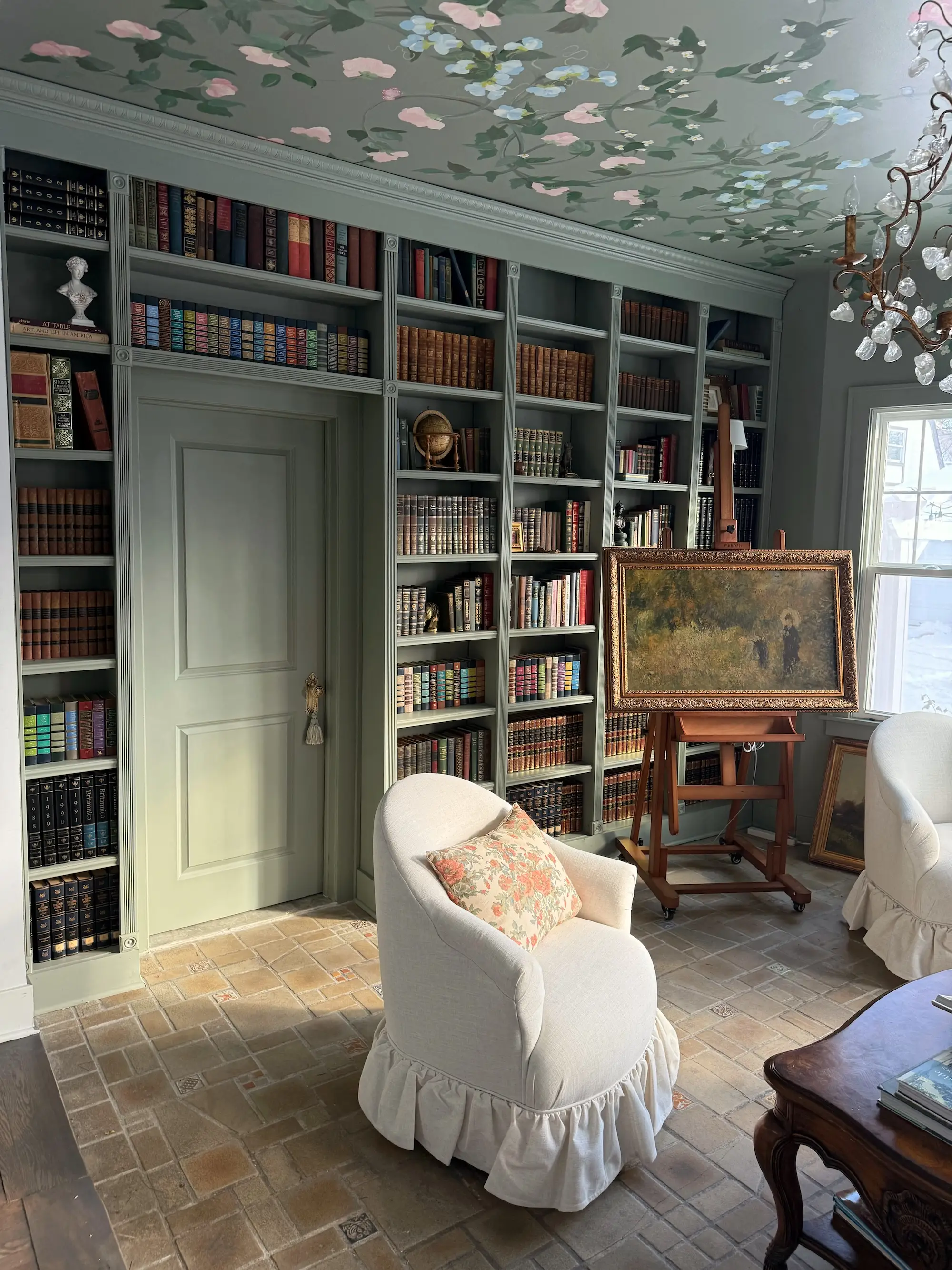 A library with green walls, built-in bookshelves, and a floral printed ceiling.