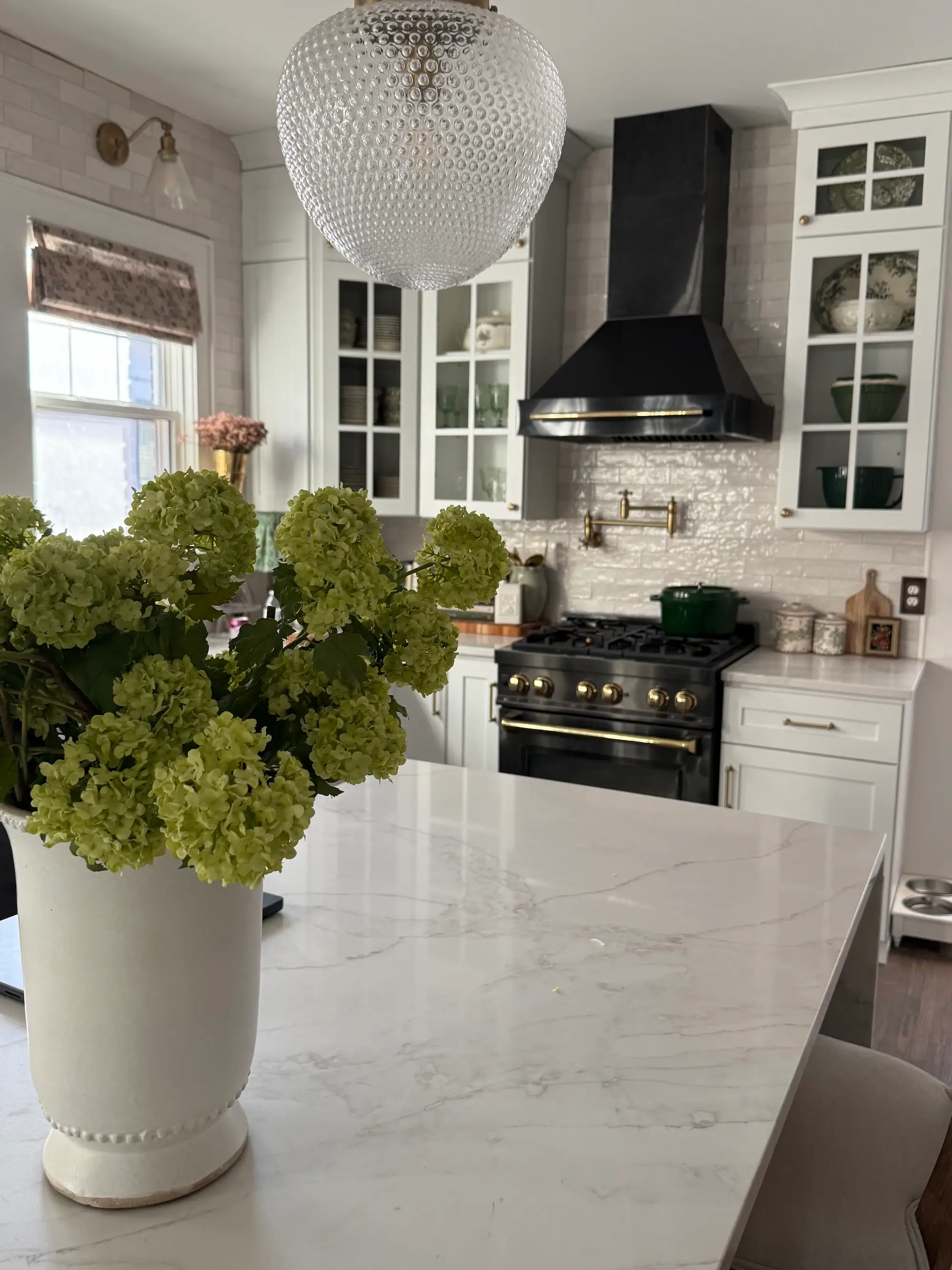 A kitchen with a large, marble island, white and glass cabinets, and a black stove.