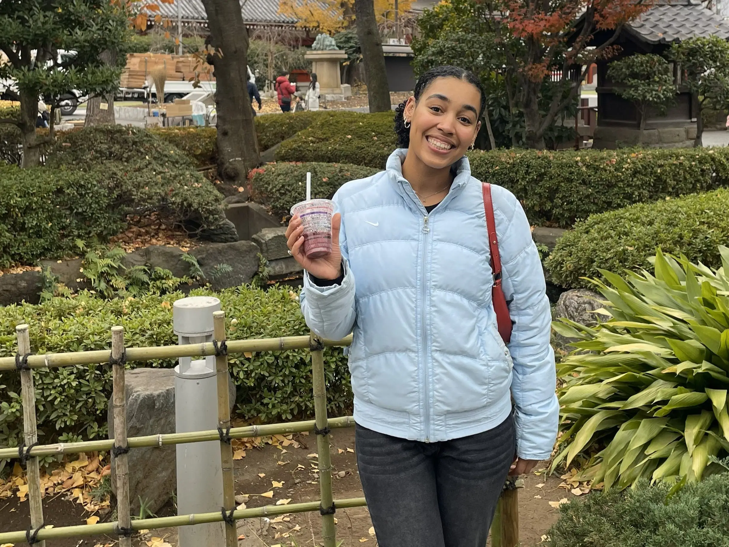 Woman smiling with drink in front of park area