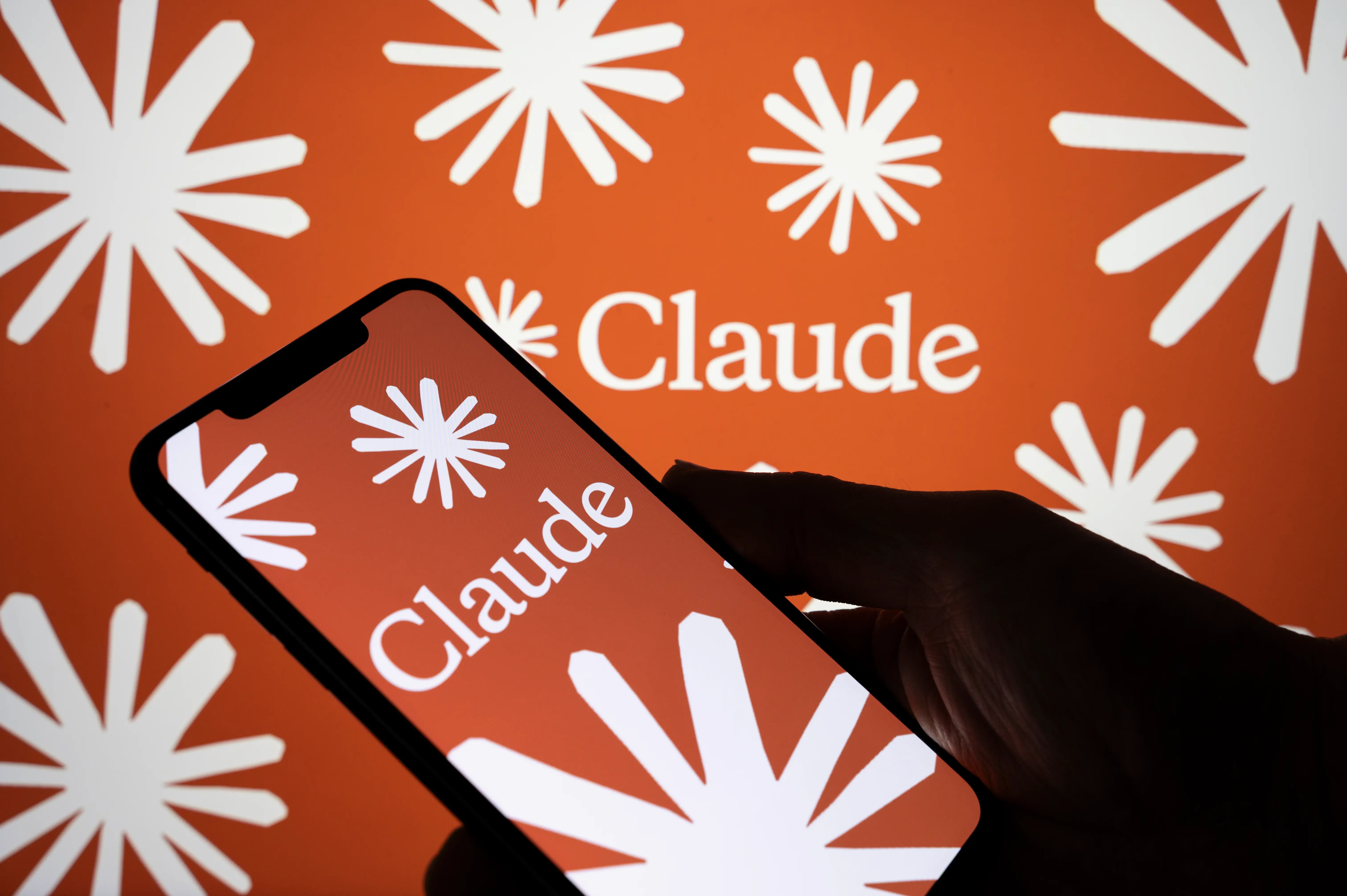 A dark figure holding a phone with Claude's emblem on the screen.