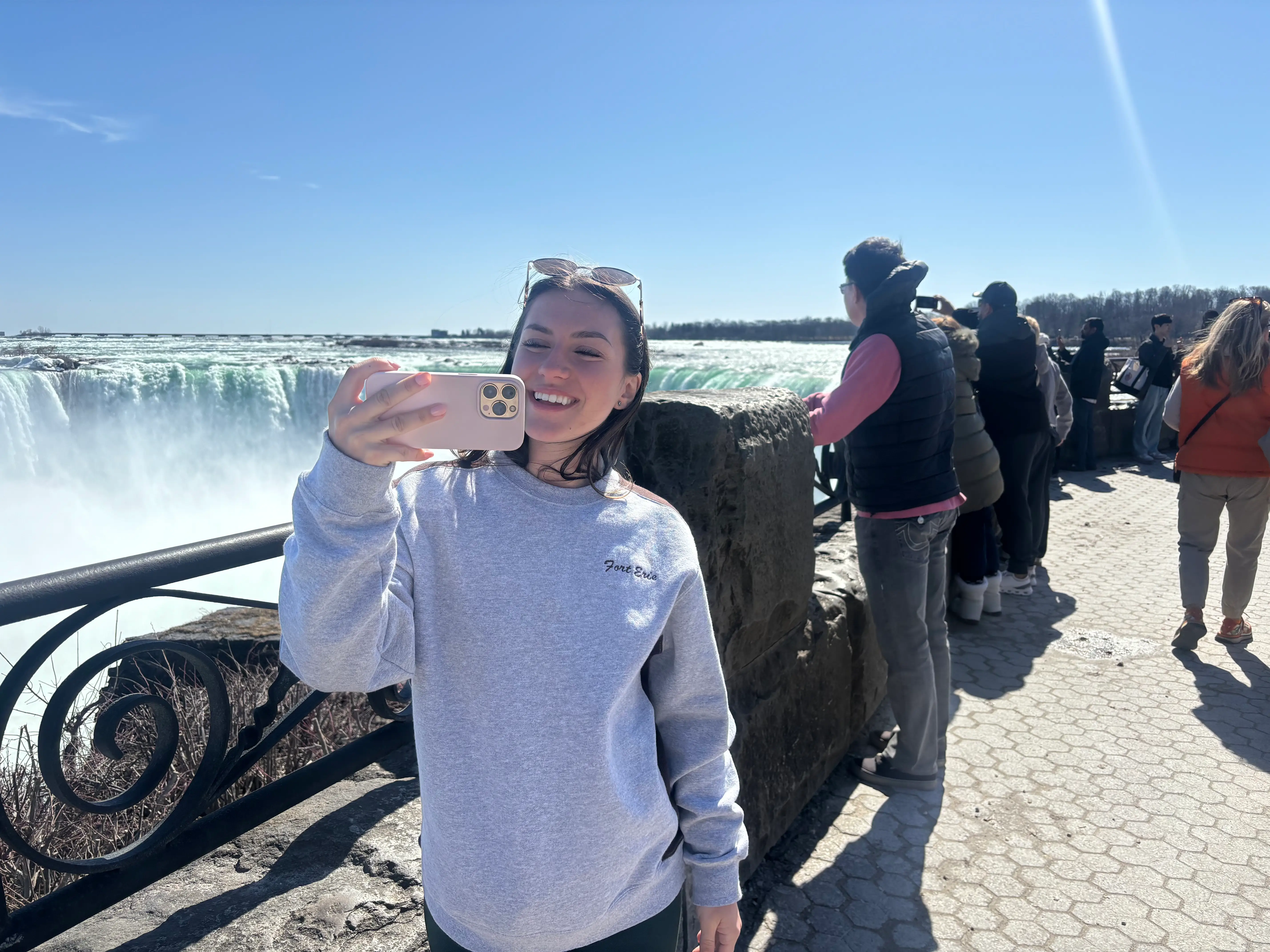 Amanda takes a selfie near the waterfall, with tourists in the background.