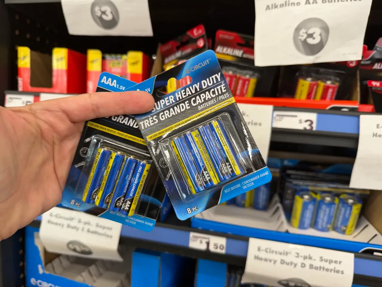 Hand holding two packs of batteries in aisle at Dollar Tree