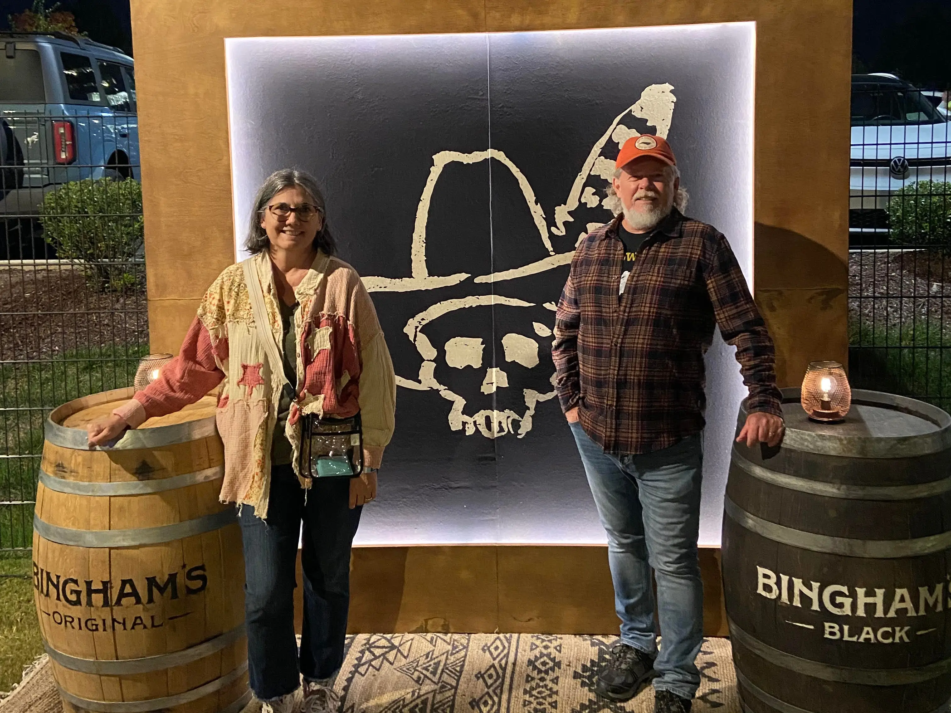 A woman and a man pose in front of a backdrop at a concert.