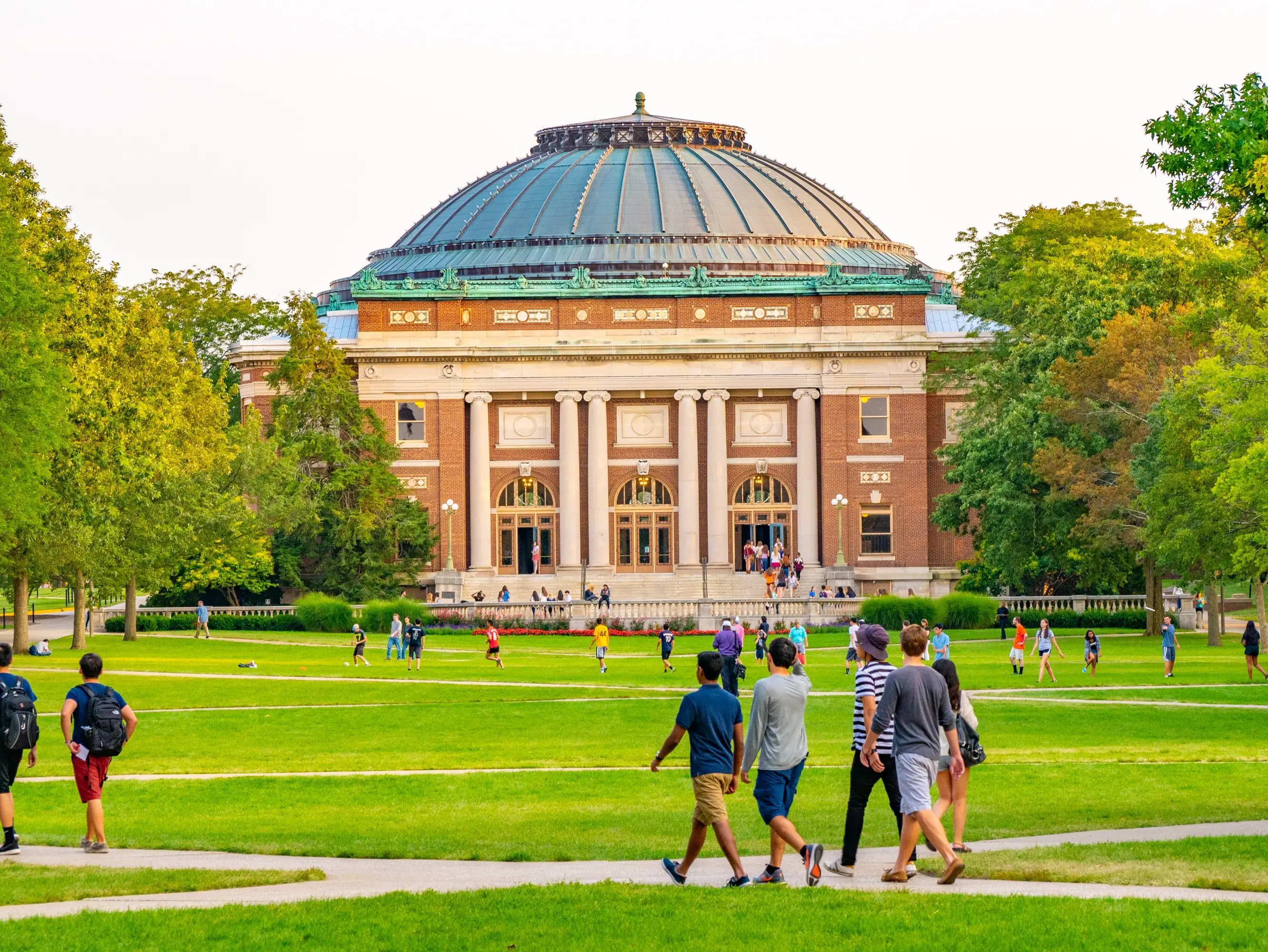 Students walk outdoors on lawn of University of Illinois college campus quad in Urbana Champaign Illinois