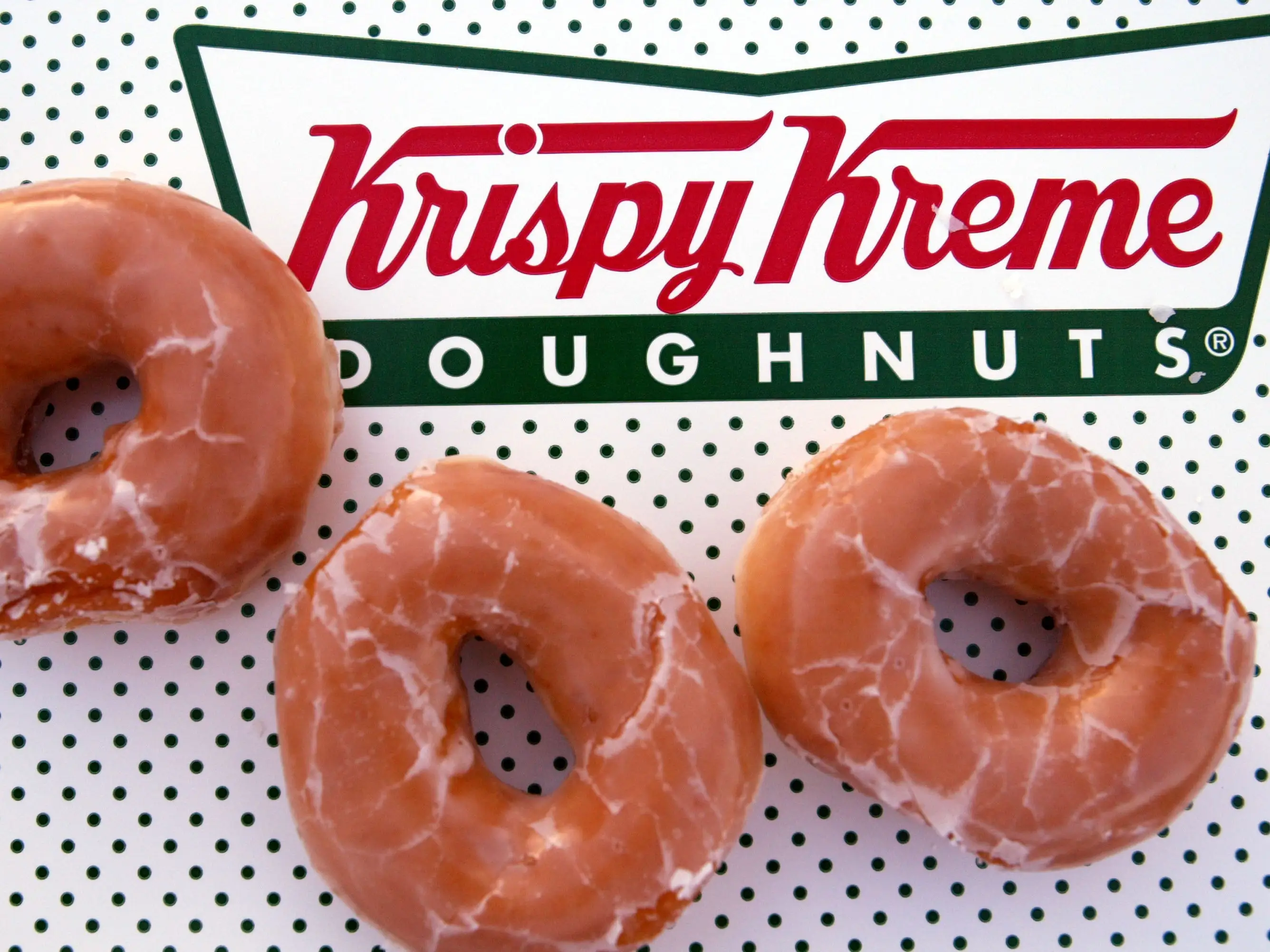 Three glazed donuts are pictured on top of a Krispy Kreme box.