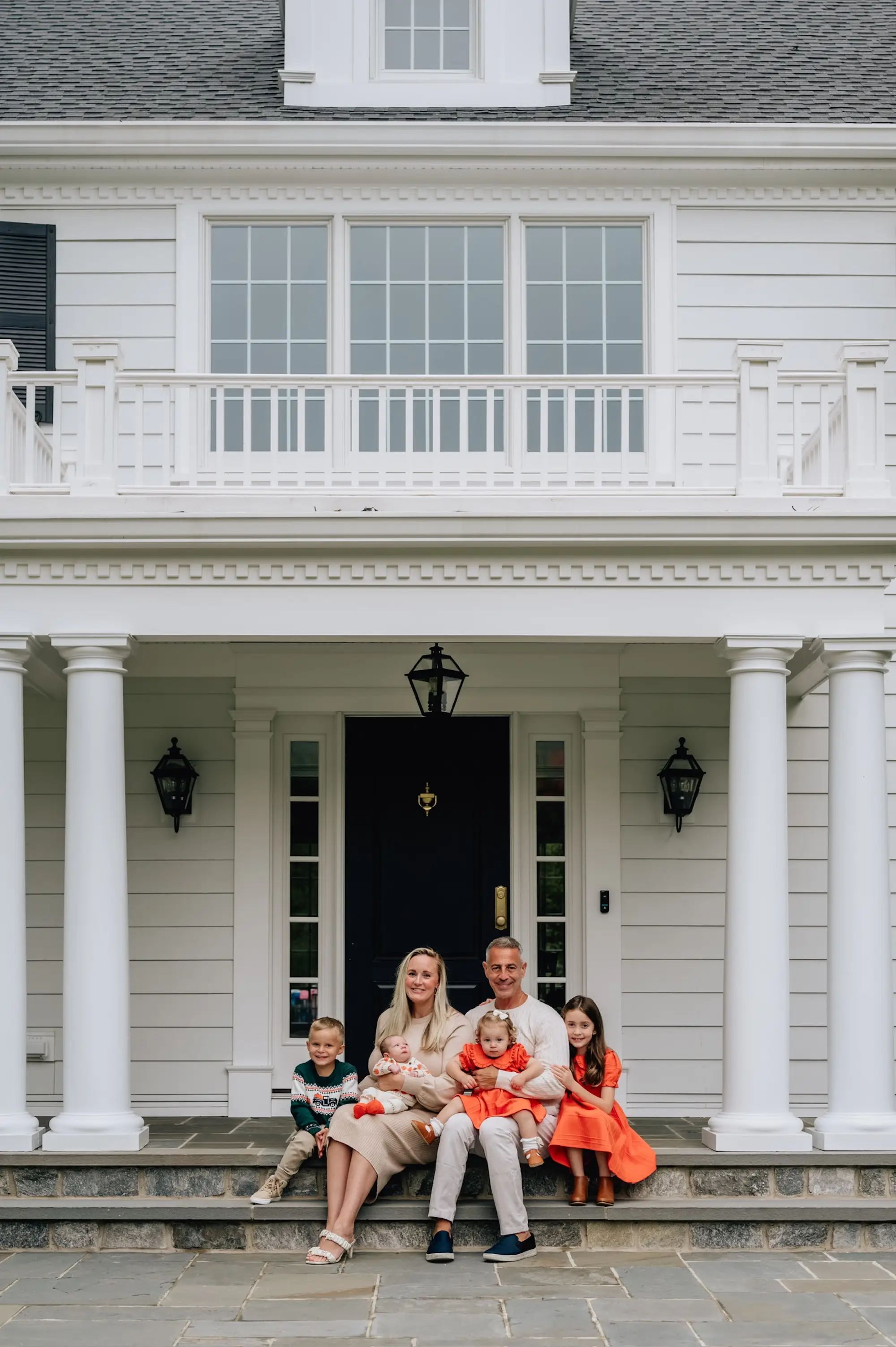 A family of five sits on the stairs in front of their white home.