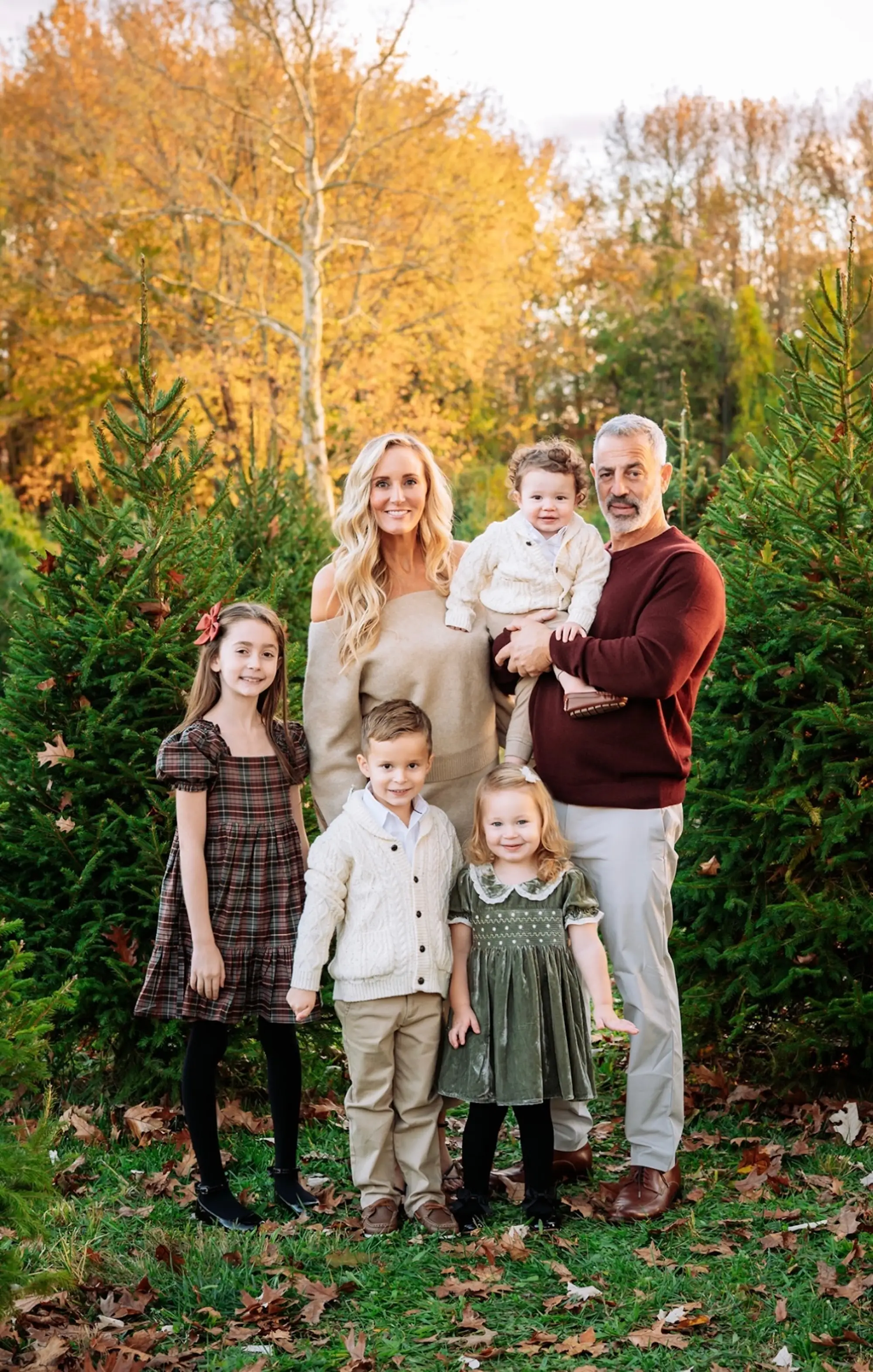 A family of five poses together and smiles in front of trees.