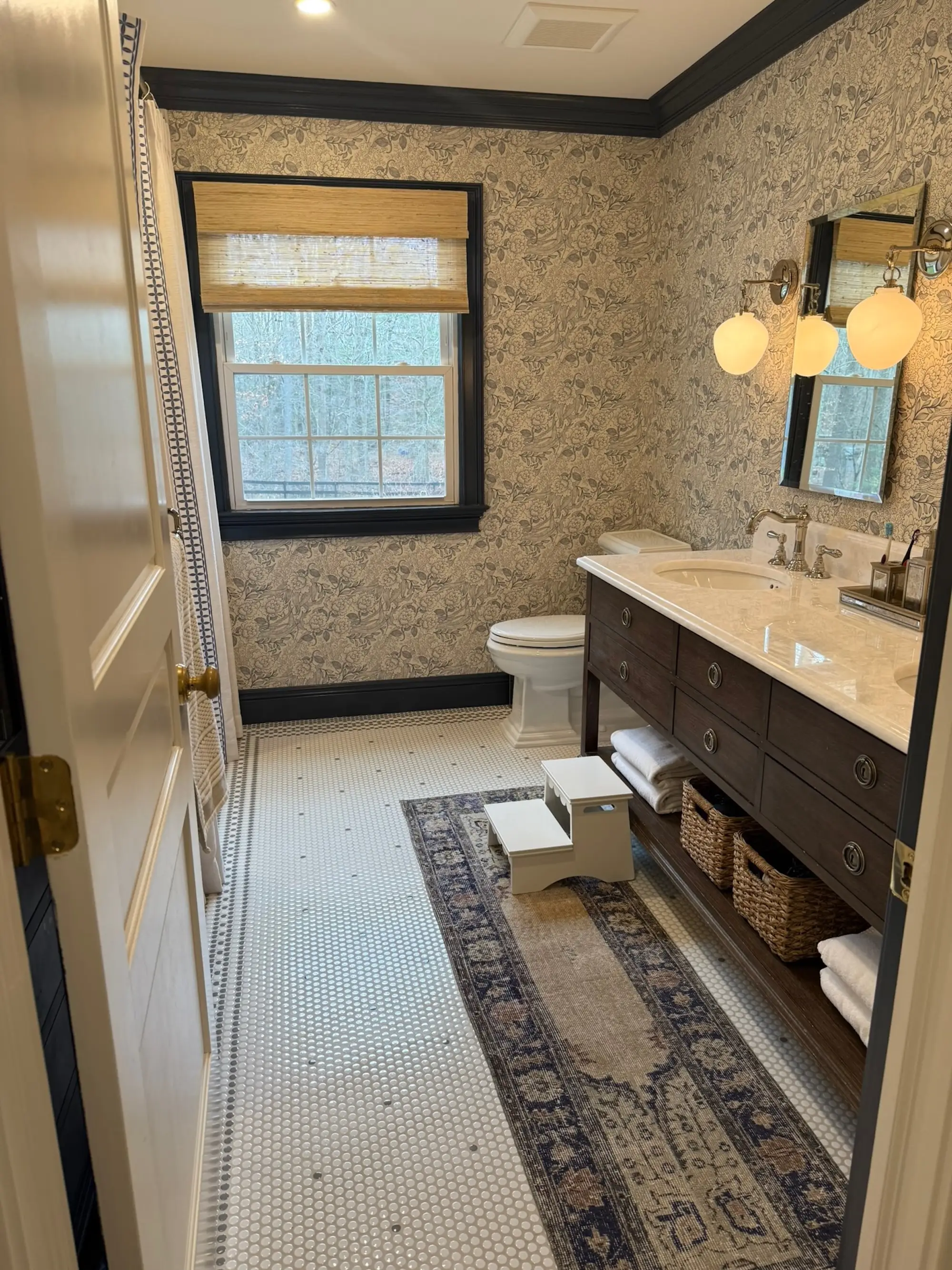 A bathroom with printed wallpaper and double vanity sinks.