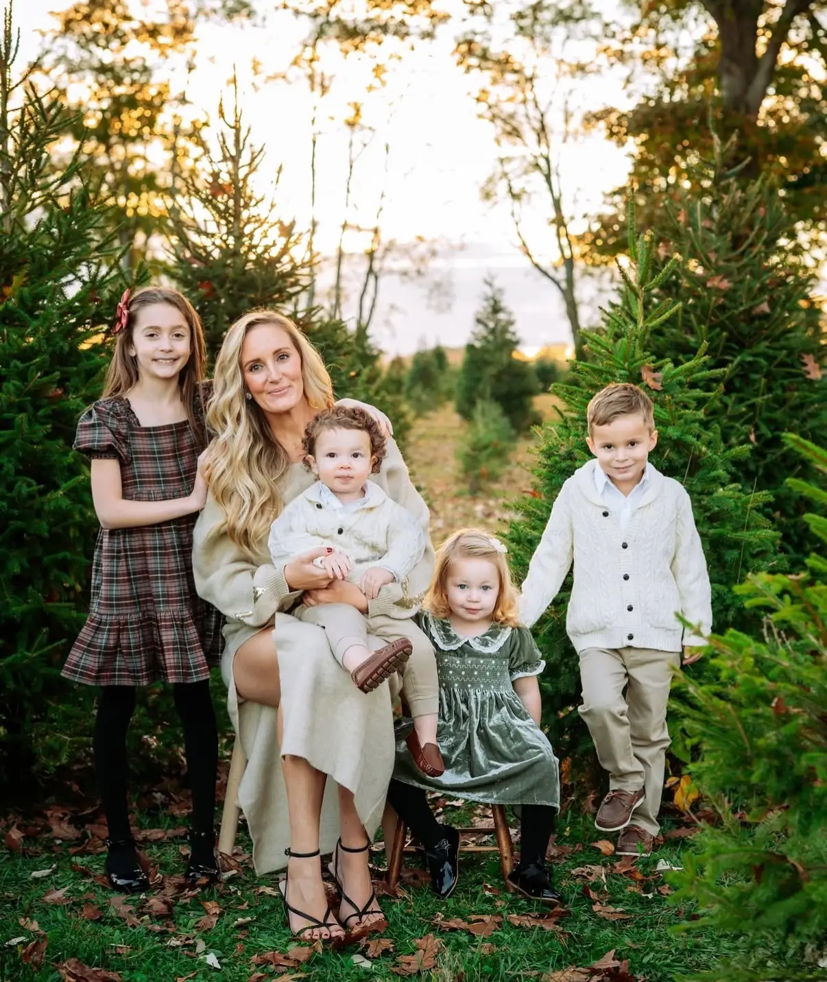 A mother poses with her four children in front of Christmas trees.