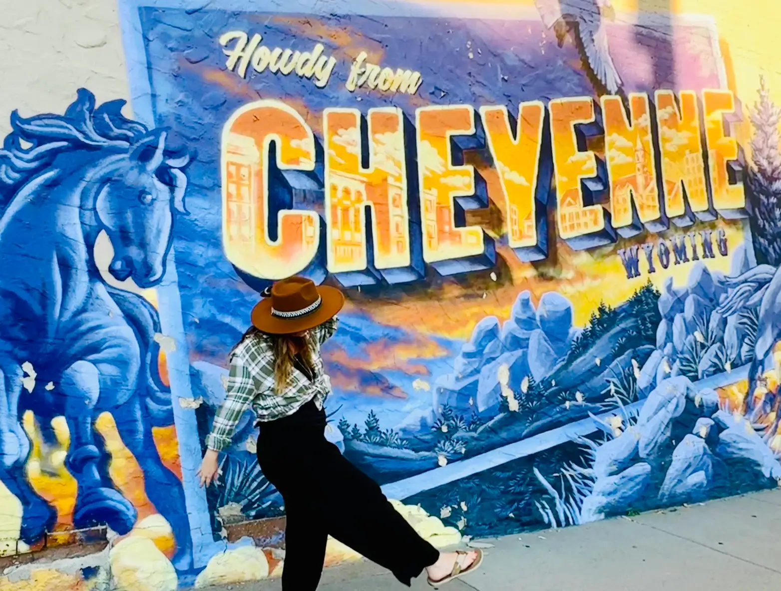 The writer posing in front of a 'Howdy from Cheyenne, Wyoming' mural.
