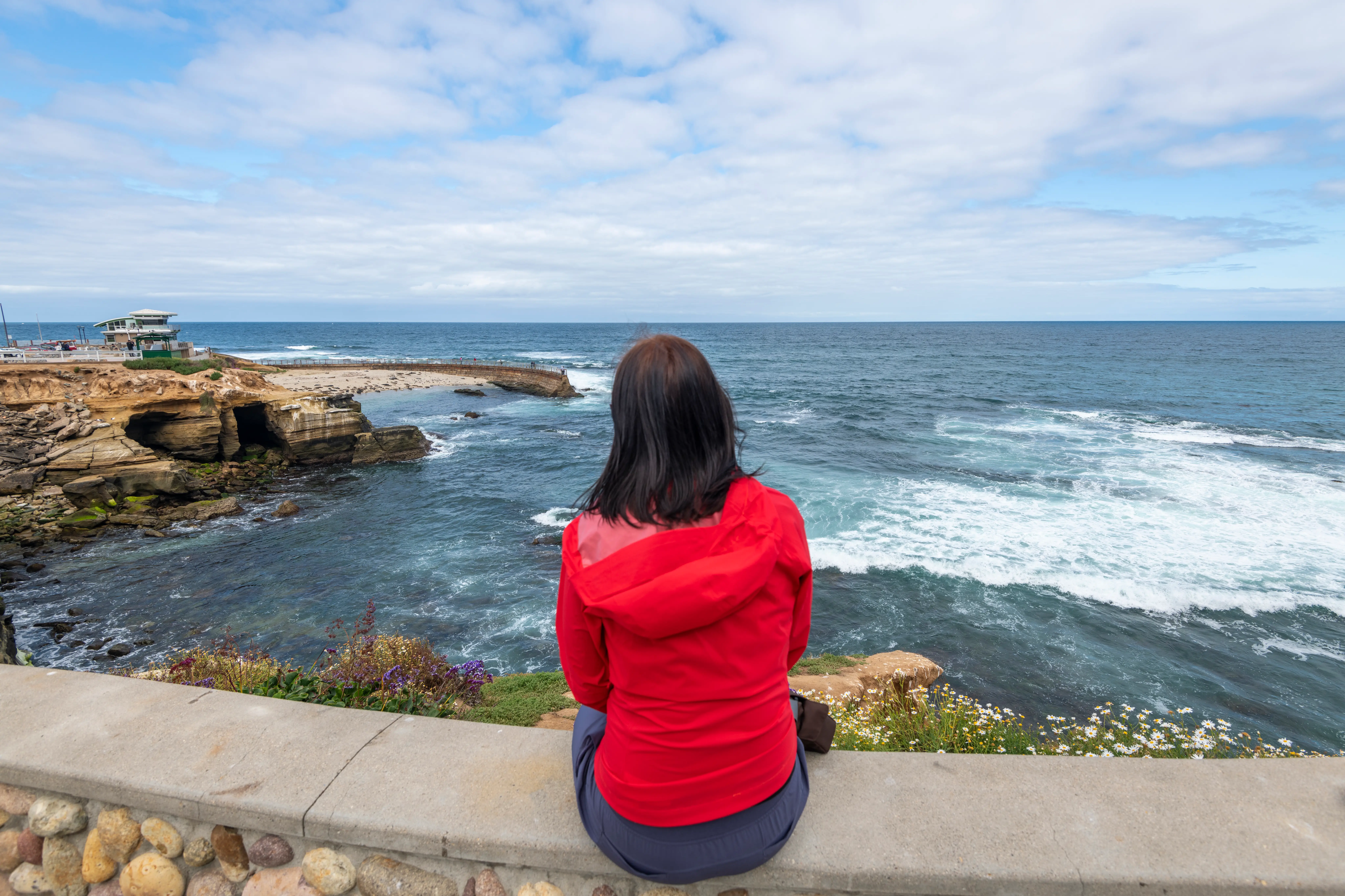 Woman staring into sea while sitting on stone ledge