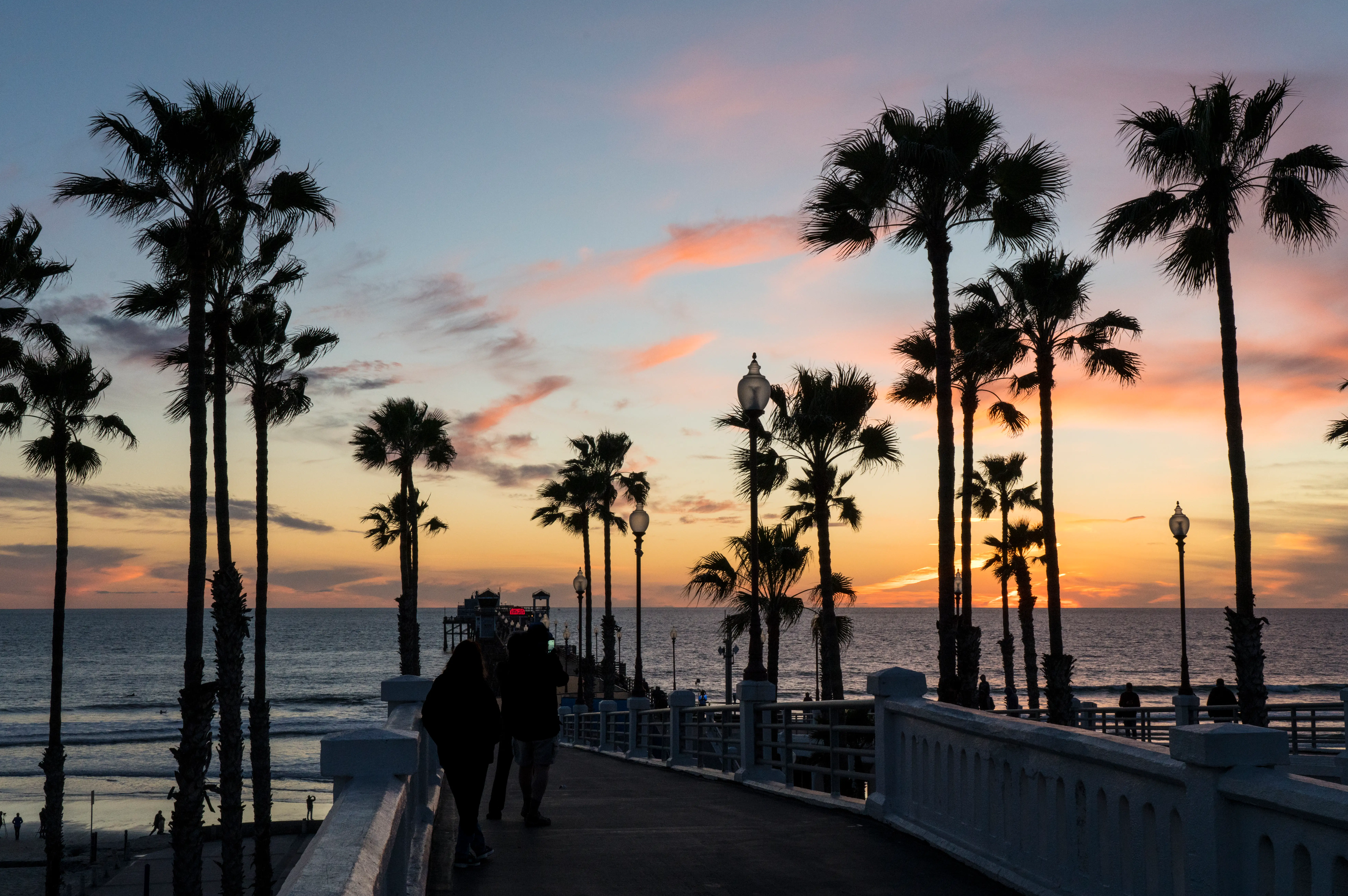 People in CAlifornia walking on pier with palm trees nearby at sunset